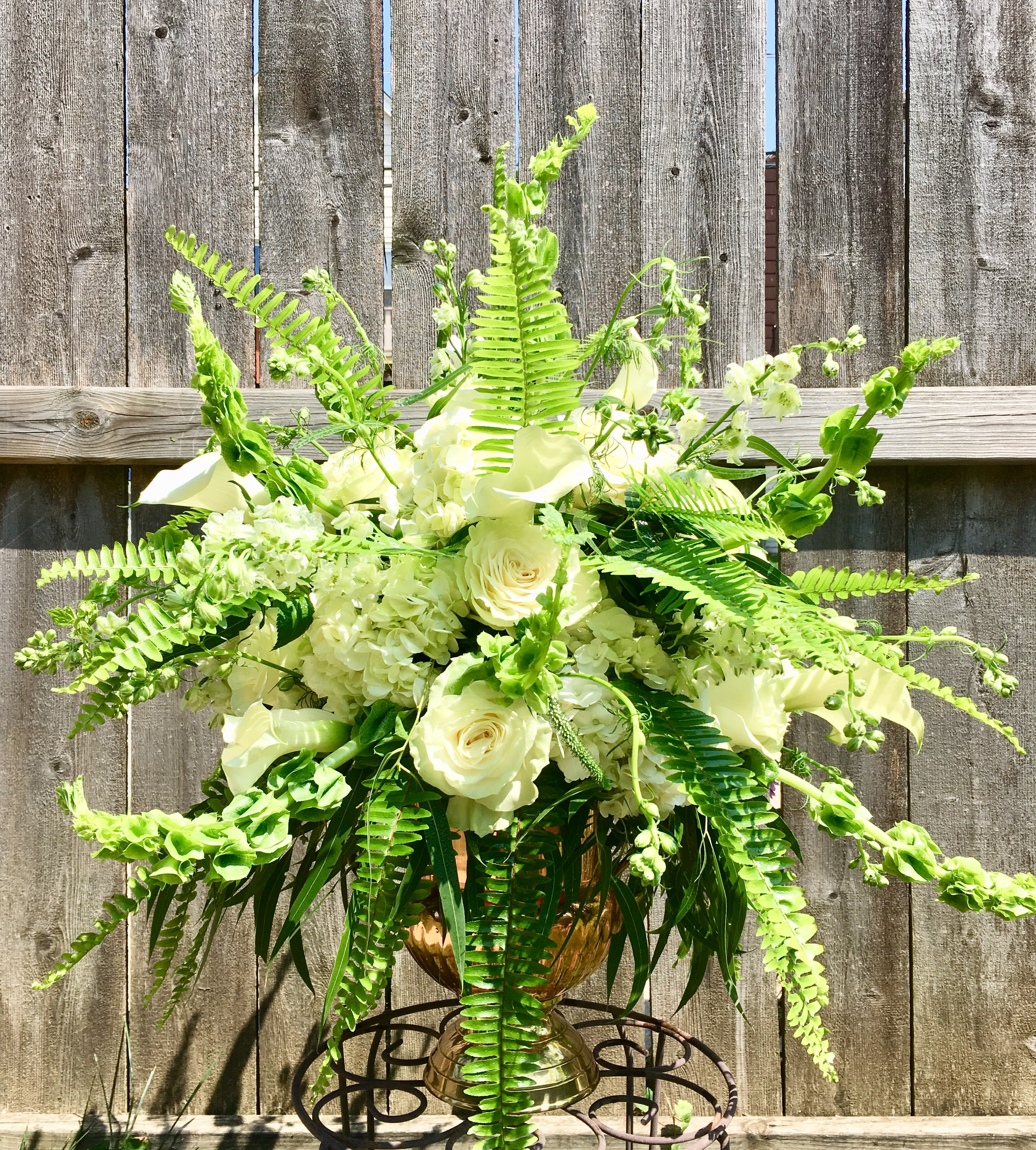 Large white rose and hydrangea arrangement with ferns in a gold urn on a metal stand