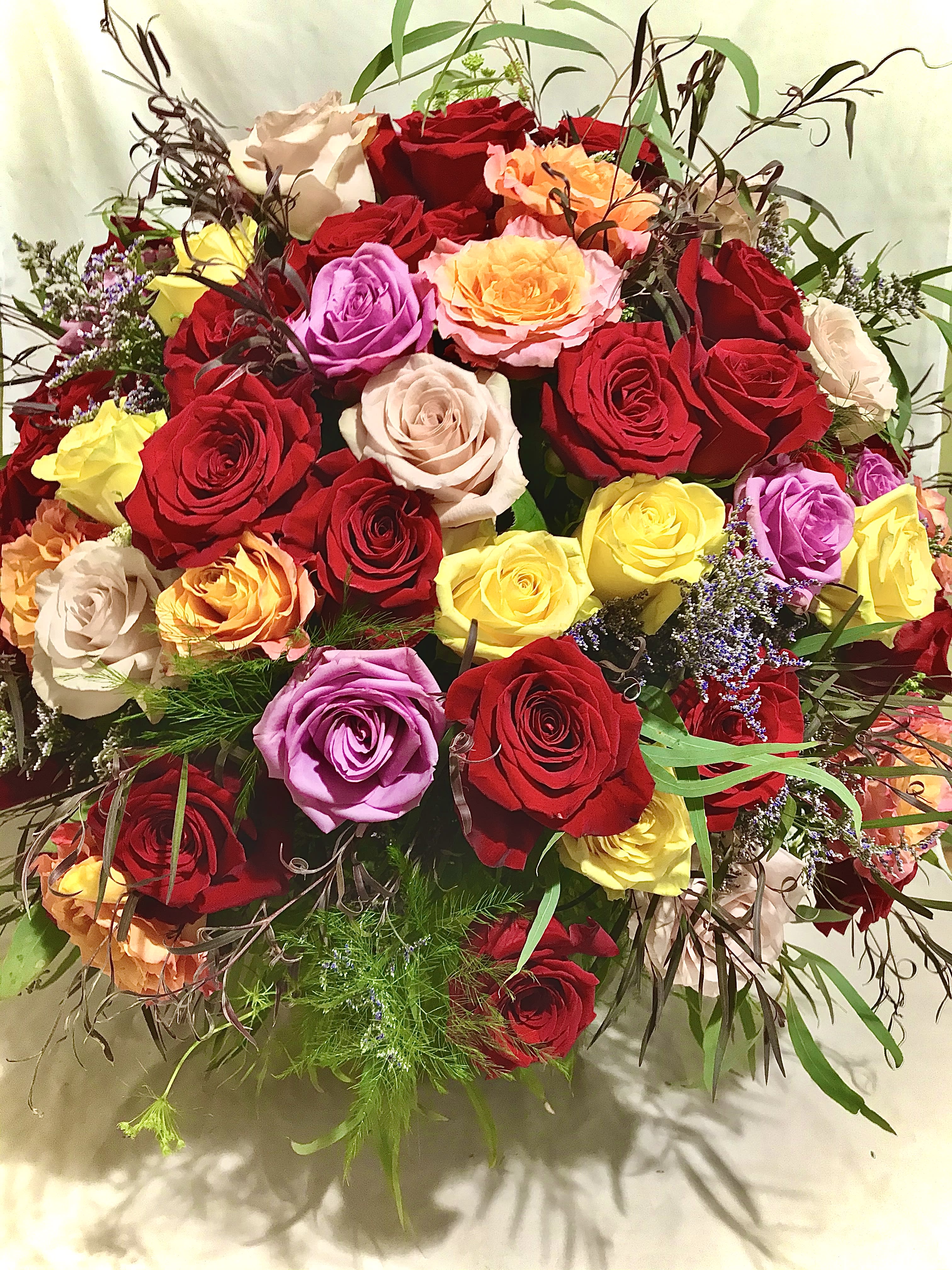 Large arrangement of mixed red, yellow, peach, and lavender roses in a rounded design