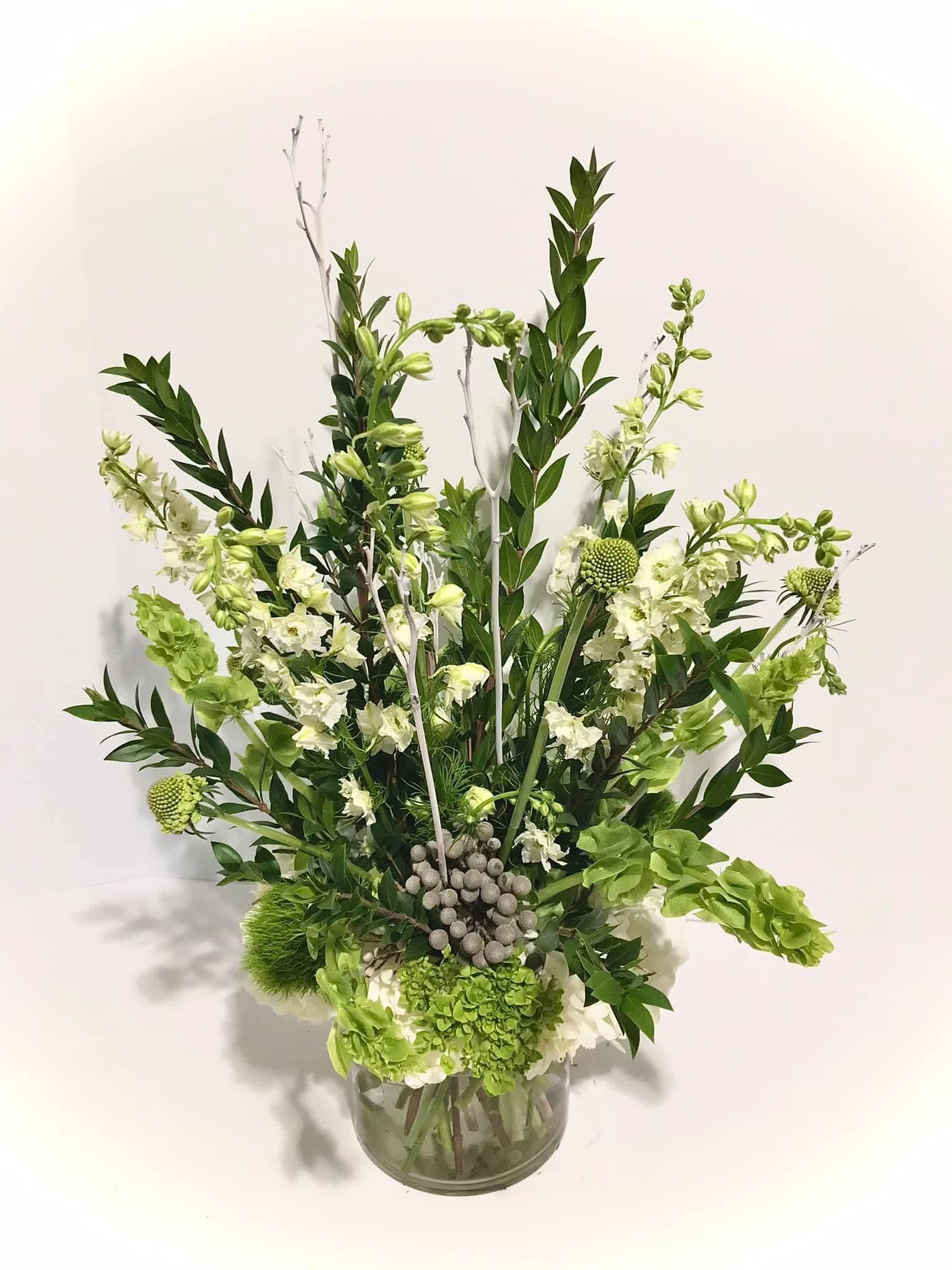 Tall green and white floral arrangement with hydrangeas and bells of Ireland in a clear glass vase.