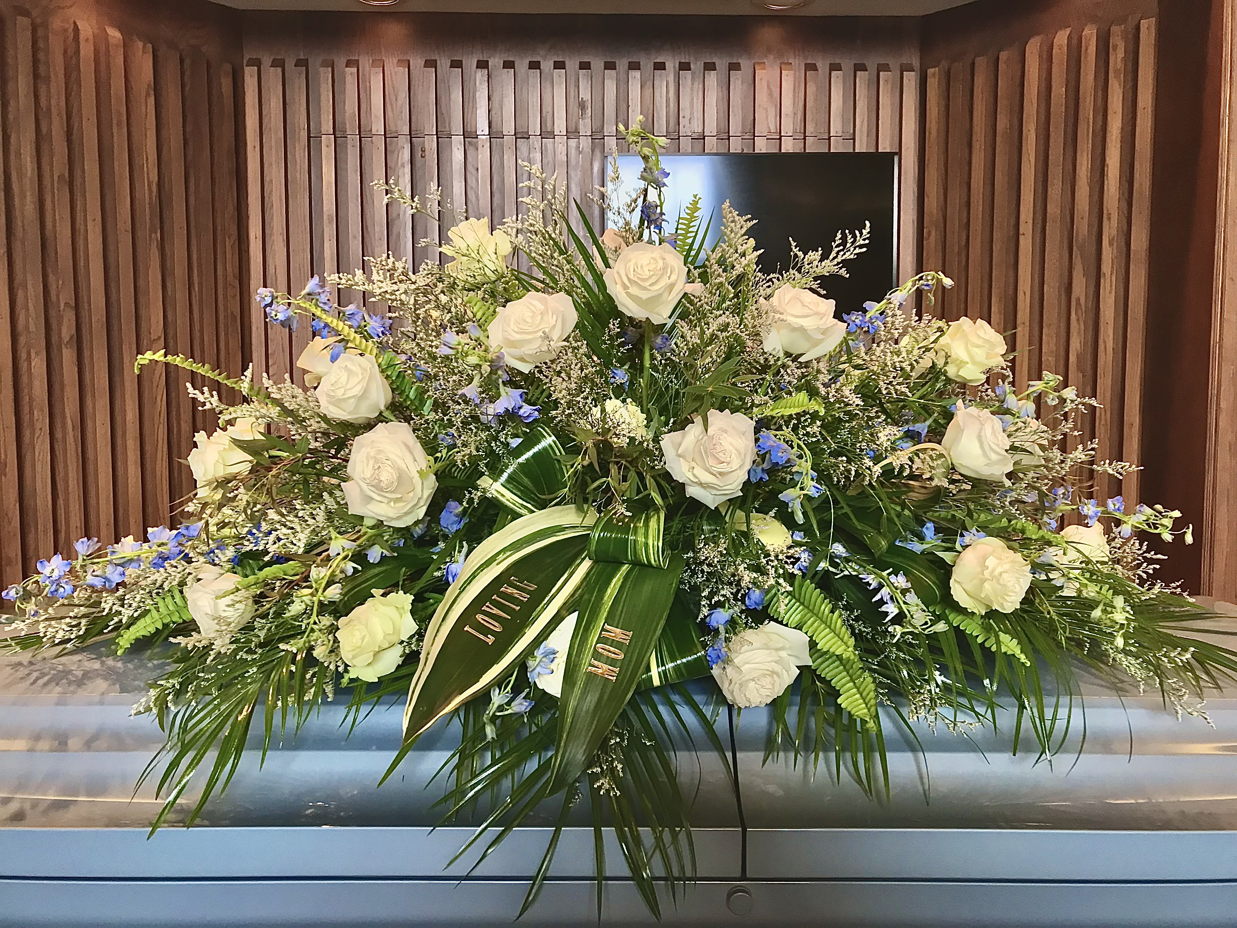Large white rose and blue flower casket spray on a silver casket