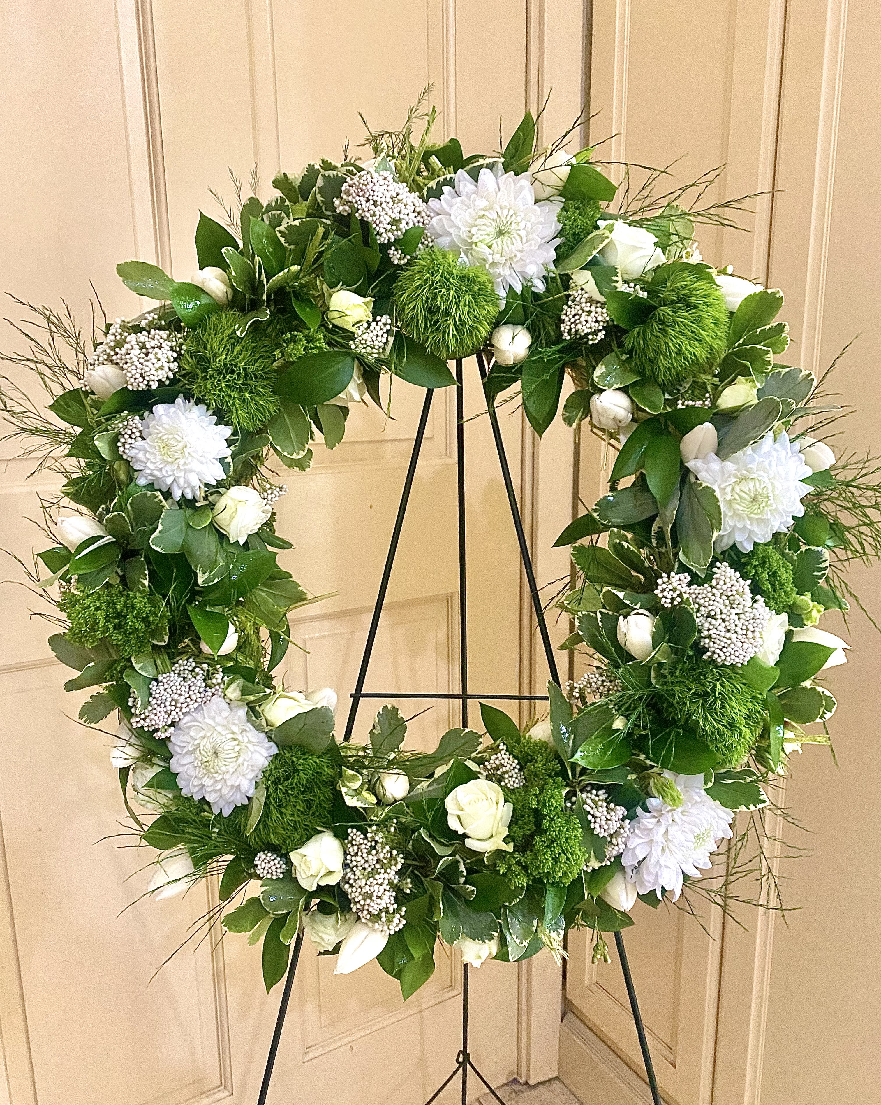Standing wreath of white flowers and green accents on a metal easel