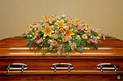 Casket spray of yellow lilies with peach and pink flowers on a polished wood casket