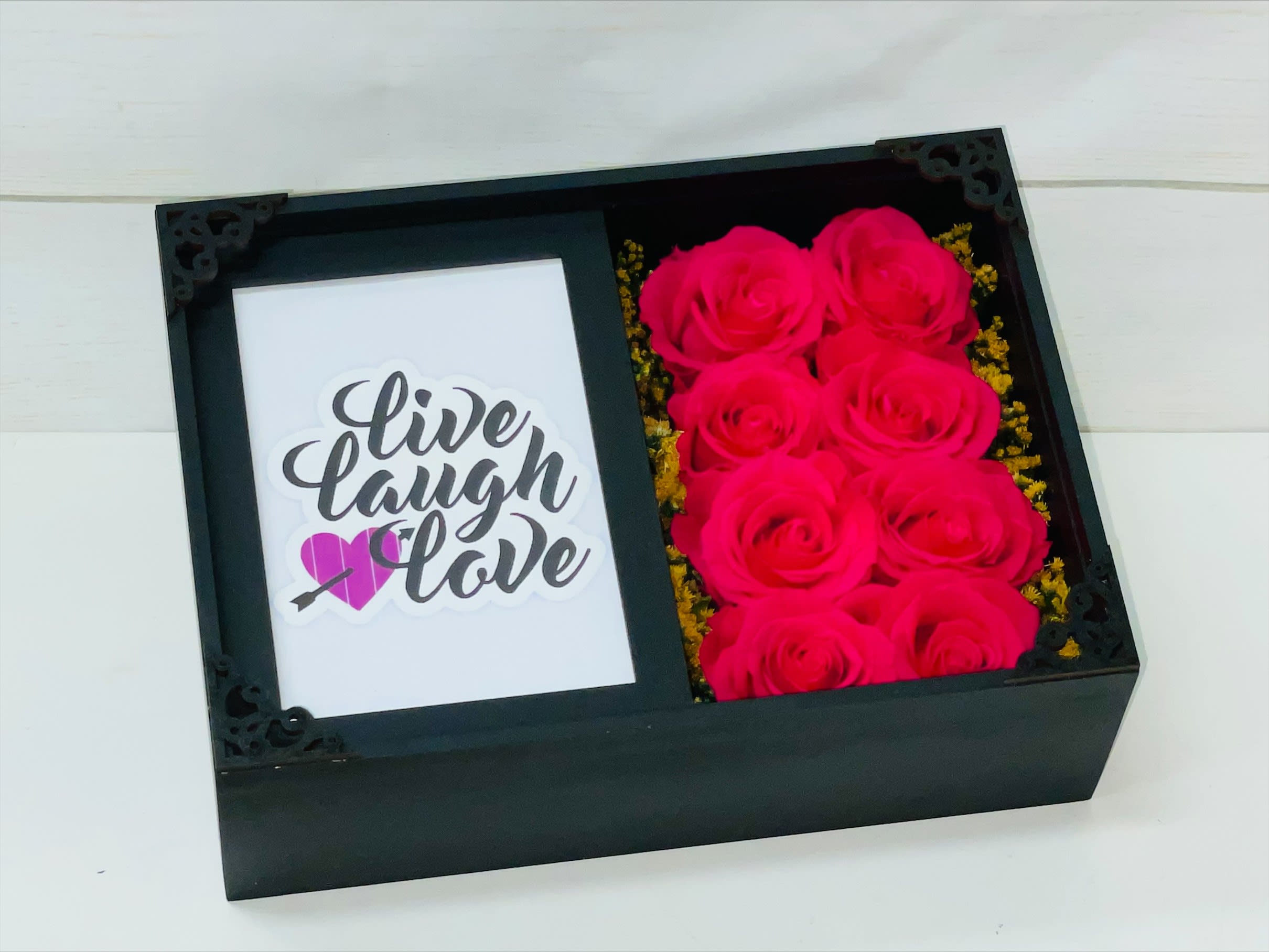 Black gift box with hot pink roses beside a card reading live laugh love