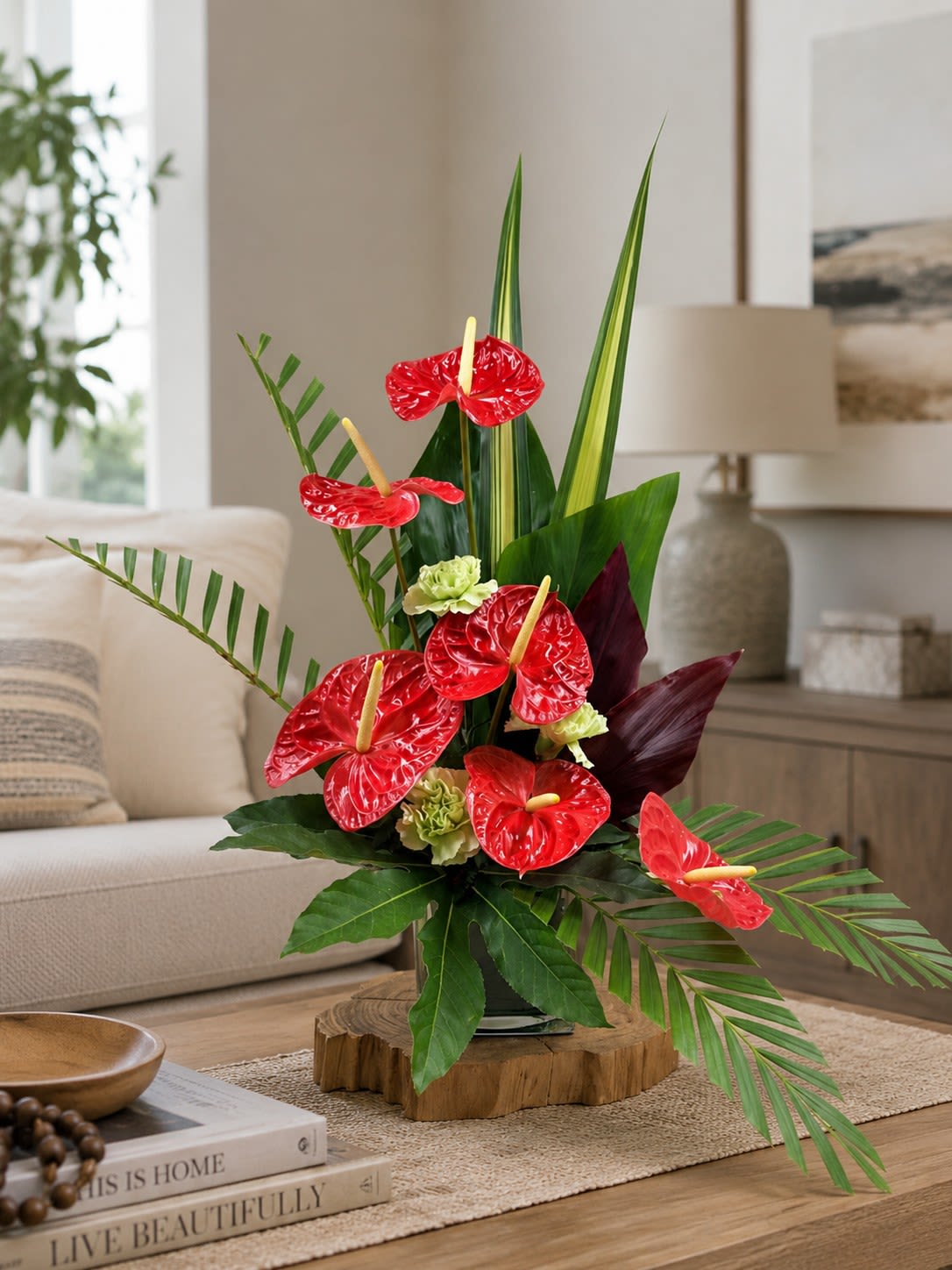 New!  Aloha Nui (Available Thursday, July 9) - Glossy red anthuriums and architectural tropical foliage give this flower arrangement an immediate wow-perfect as a housewarming centerpiece, birthday bouquet, or bold everyday celebration piece. The upright, sculptural silhouette reads modern and exotic; the person you're sending it to will feel noticed and delighted by the striking red-and-green contrast and dramatic fan-like fronds.  This composition pairs several bright red anthuriums with long palm fronds, broad glossy leaves, and small pale green accent blooms, with touches of deep burgundy foliage for depth. It's presented in a clear glass vase for a clean, contemporary look that dresses up mantels, dining tables, or entry consoles. The vertical design stands out visually while remaining neat and easy to place.  Aloha Nui is an expressive choice for someone who loves tropical style-ideal for celebrating a new home, marking a birthday, or saying thanks in a way that feels thoughtfully curated. For best results, follow the included care and handling QR code for watering and placement tips so the arrangement maintains its dramatic shape and long-lasting color.