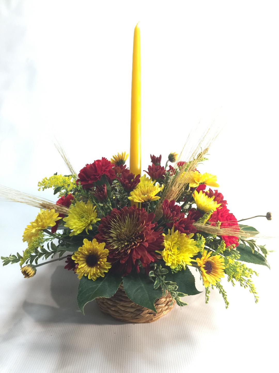 Basket arrangement of yellow and red flowers with a tall yellow candle