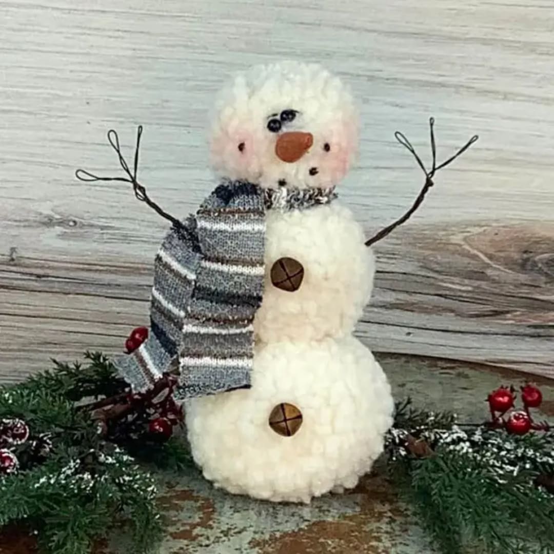 Small plush snowman with a striped scarf and wire arms on a rustic surface