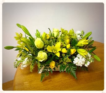 Yellow lilies and roses arranged with white flowers in a low centerpiece