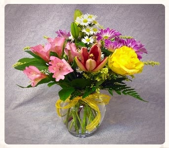 Mixed bouquet of pink, yellow, and purple flowers in a glass vase