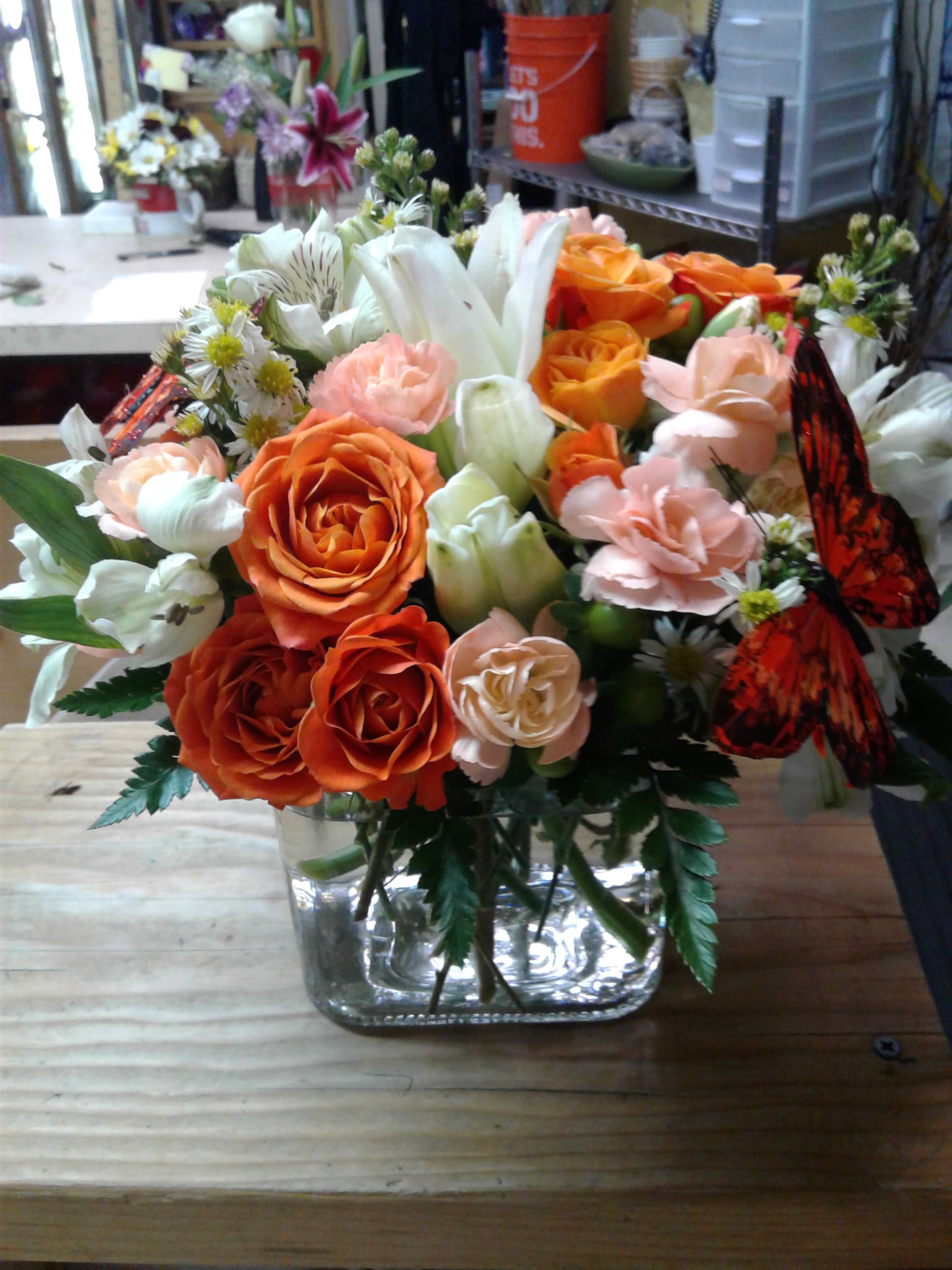 Orange and peach rose bouquet in a clear glass vase with white lilies