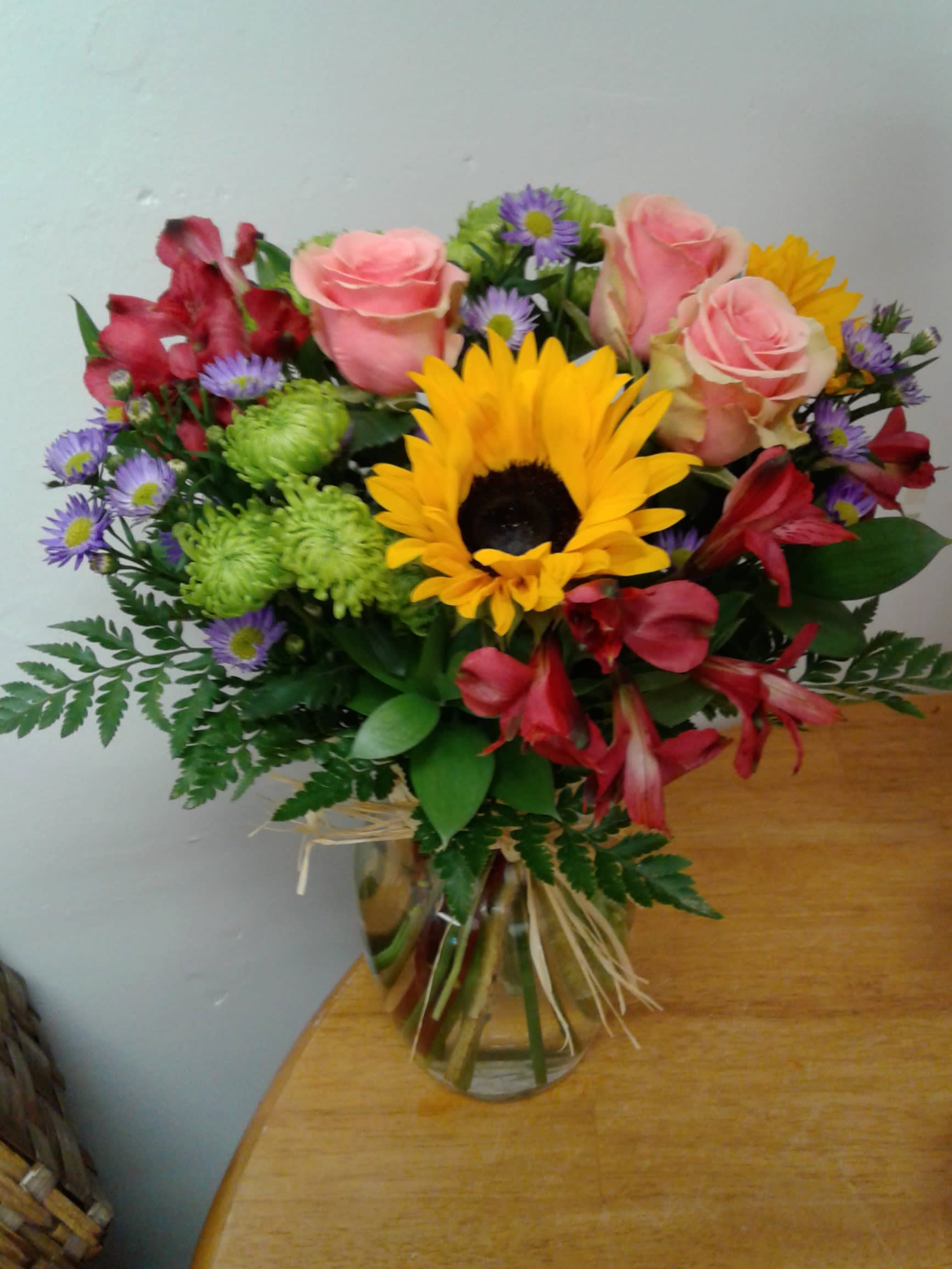 Bouquet of pink roses, a sunflower, and mixed blooms in a glass vase