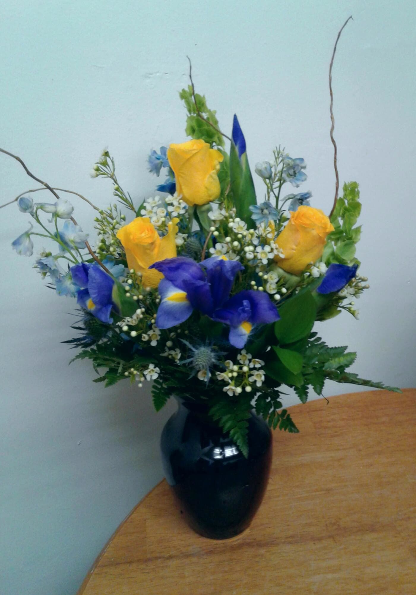 Yellow roses and blue irises in a black vase