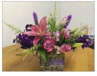 Pink lilies and roses in a glass vase with purple accents