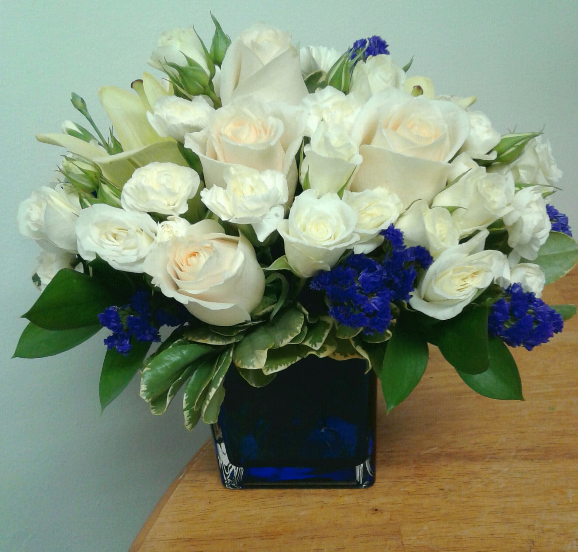 White roses and calla lilies arranged in a blue glass vase