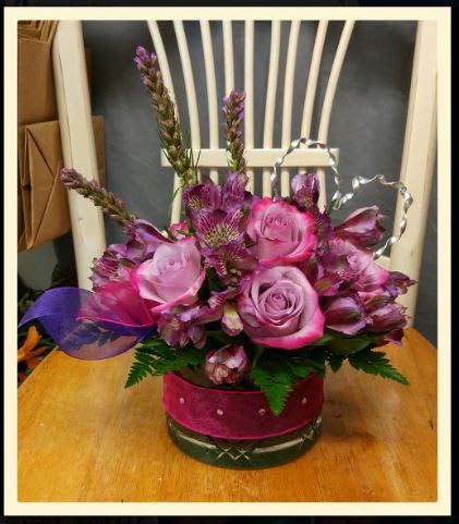 Pink roses and purple flowers arranged in a round glass vase
