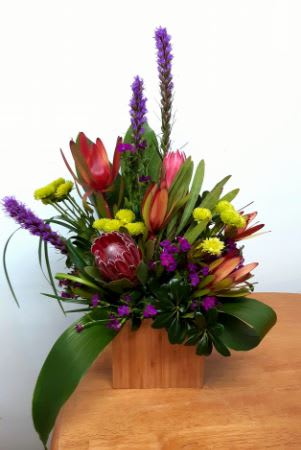 Tropical floral arrangement with purple spikes and red-orange blooms in a wooden box