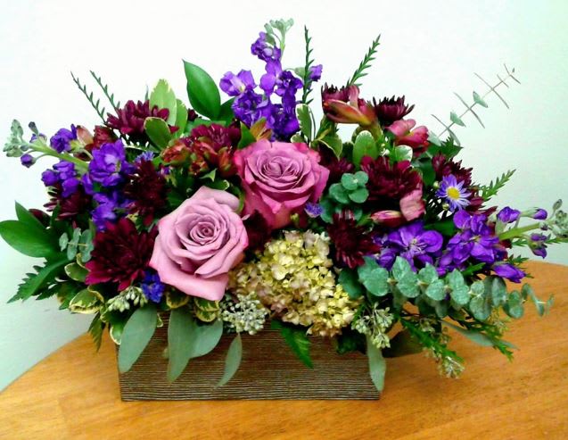 Mixed bouquet with pink roses and purple flowers in a rectangular wooden container