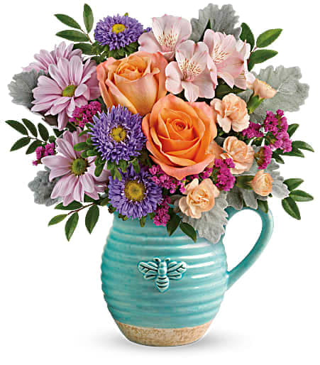 Bouquet of peach roses, pink daisies, and purple flowers in a turquoise pitcher vase