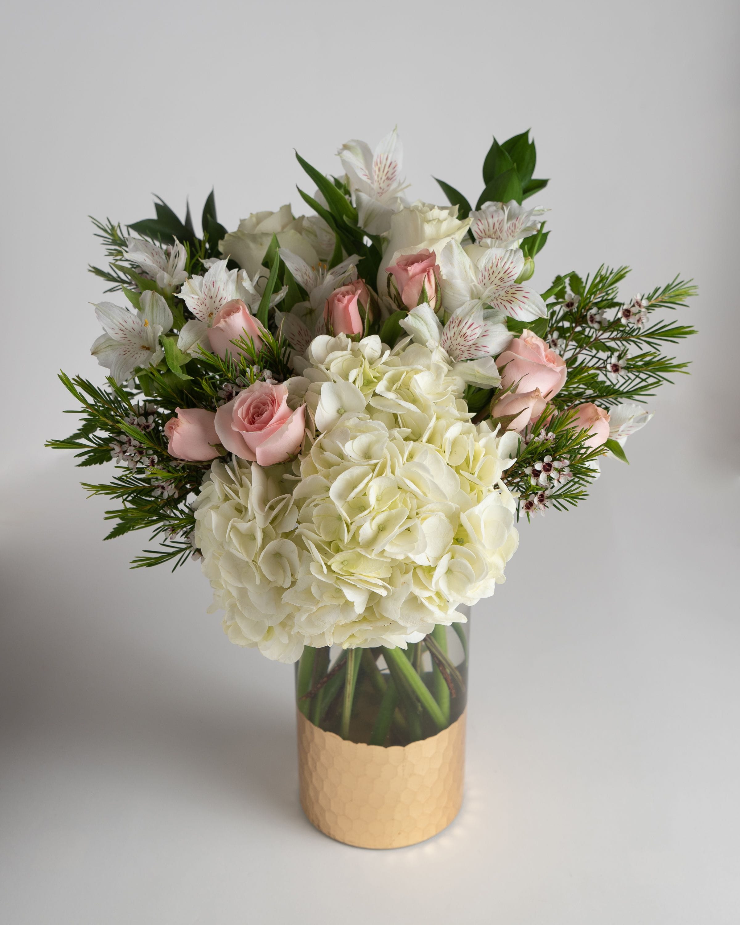 White hydrangeas and pink roses in a glass vase with greenery