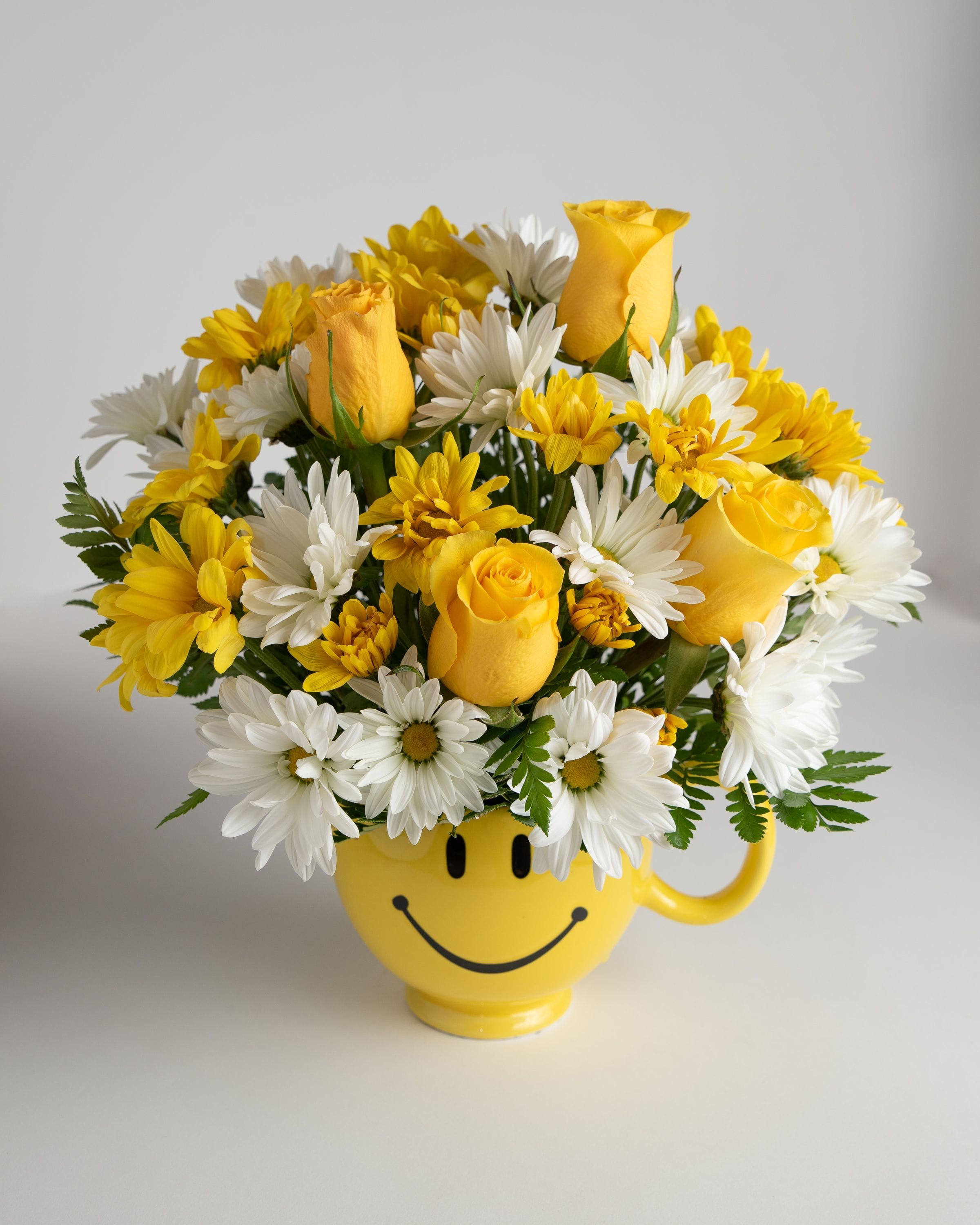 Yellow roses and white daisies in a smiley-face mug