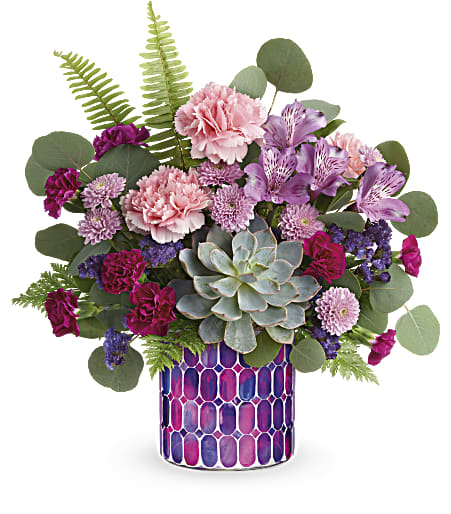 Mixed pink and purple flowers in a patterned vase with a succulent centerpiece