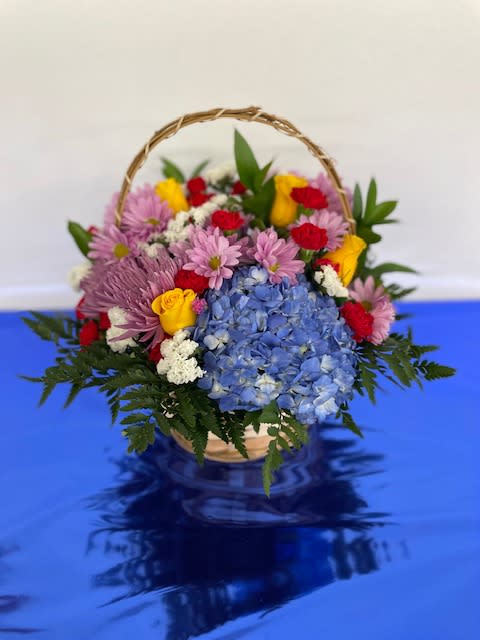 Basket arrangement of blue hydrangeas, pink daisies, and yellow roses