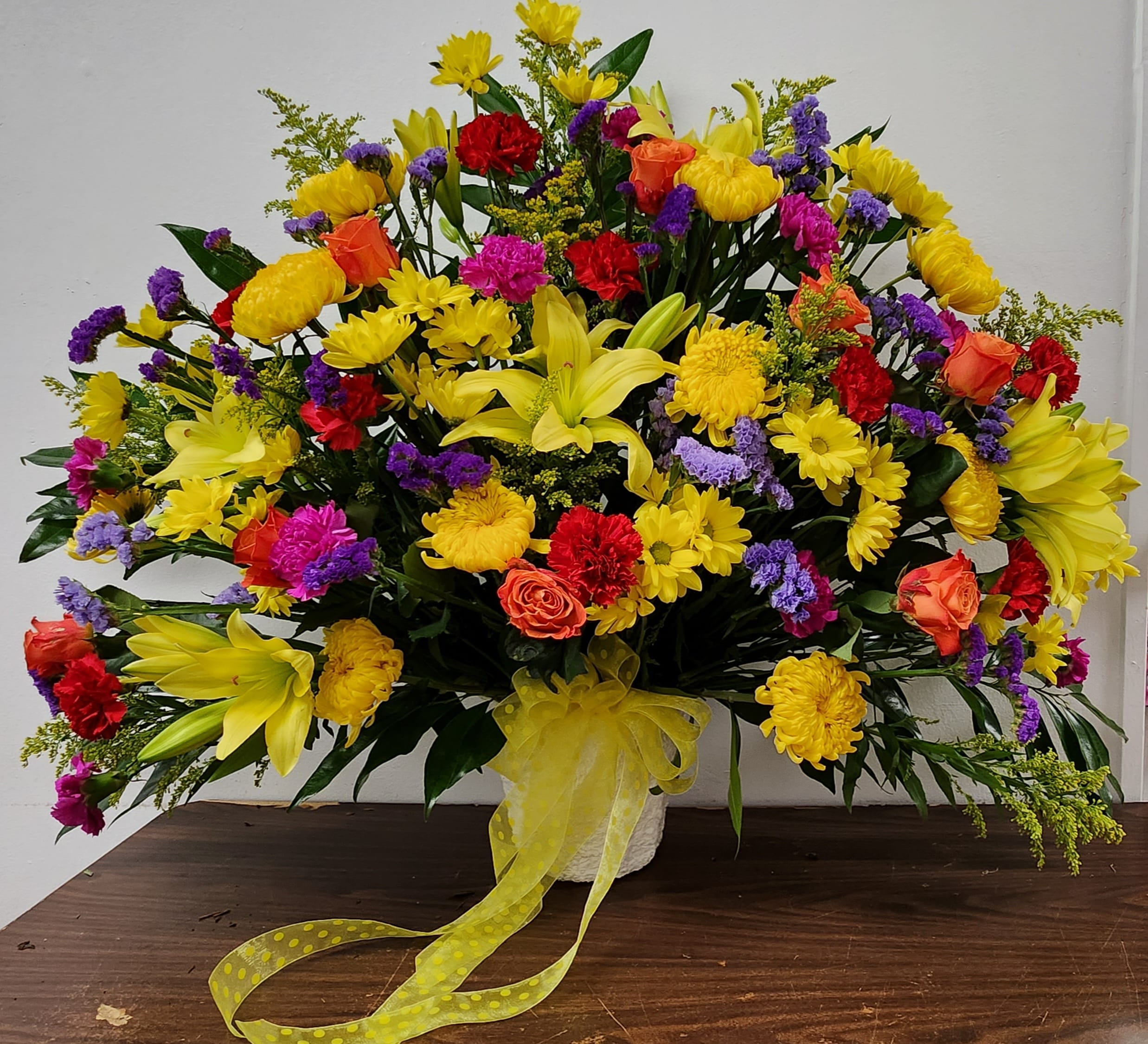 Large mixed bouquet with yellow lilies, roses, and daisies in a white vase