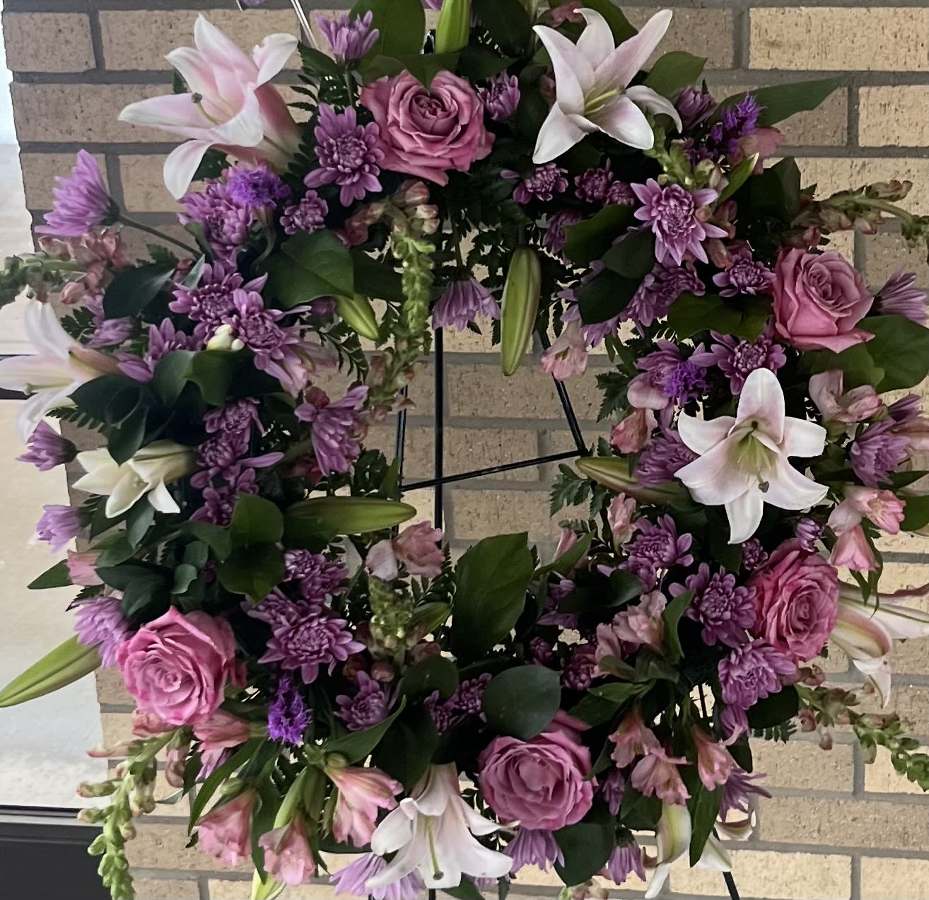 Round floral wreath with pink roses, white lilies, and purple blooms