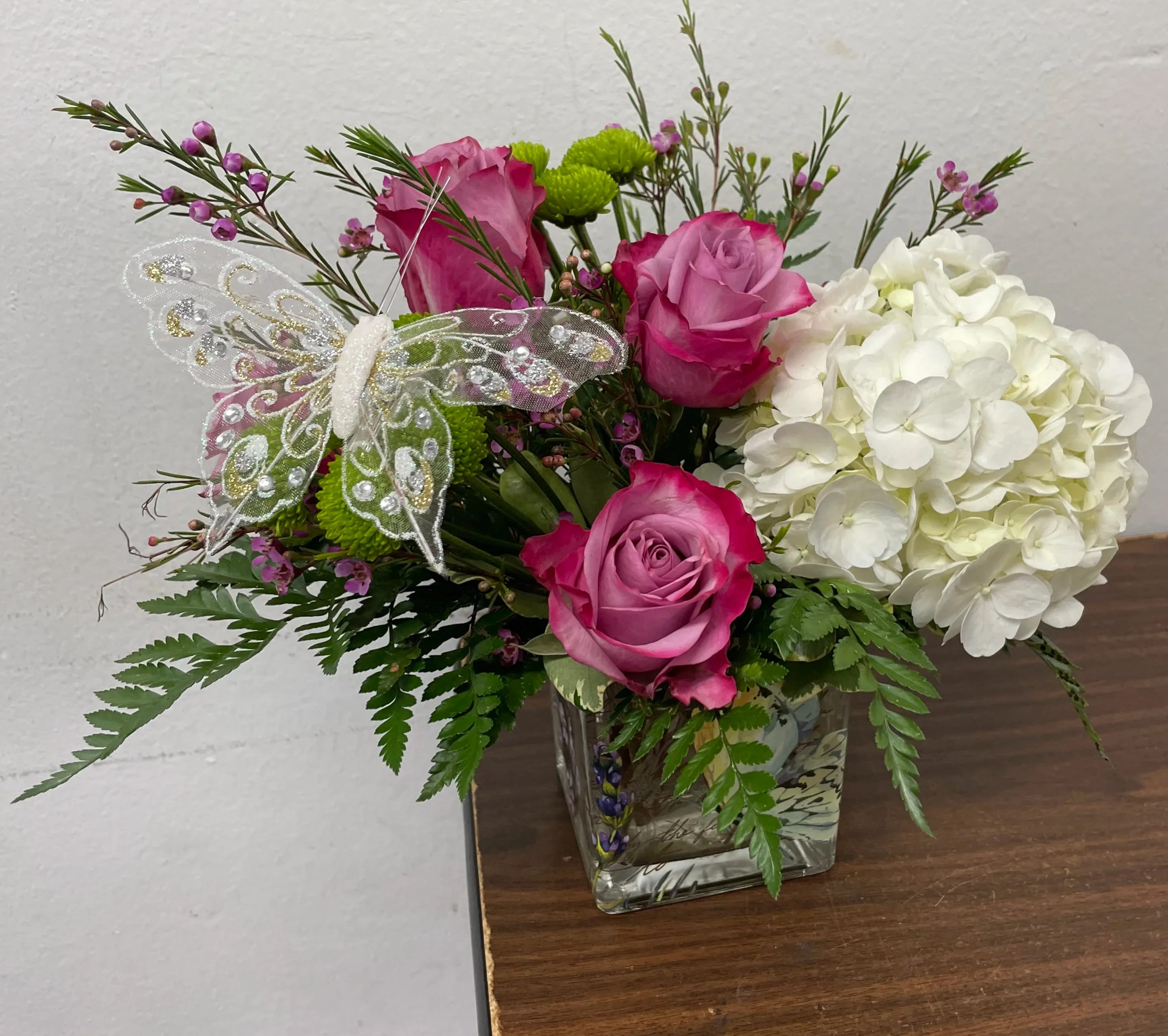 Pink roses and white hydrangea in a glass vase with a decorative butterfly