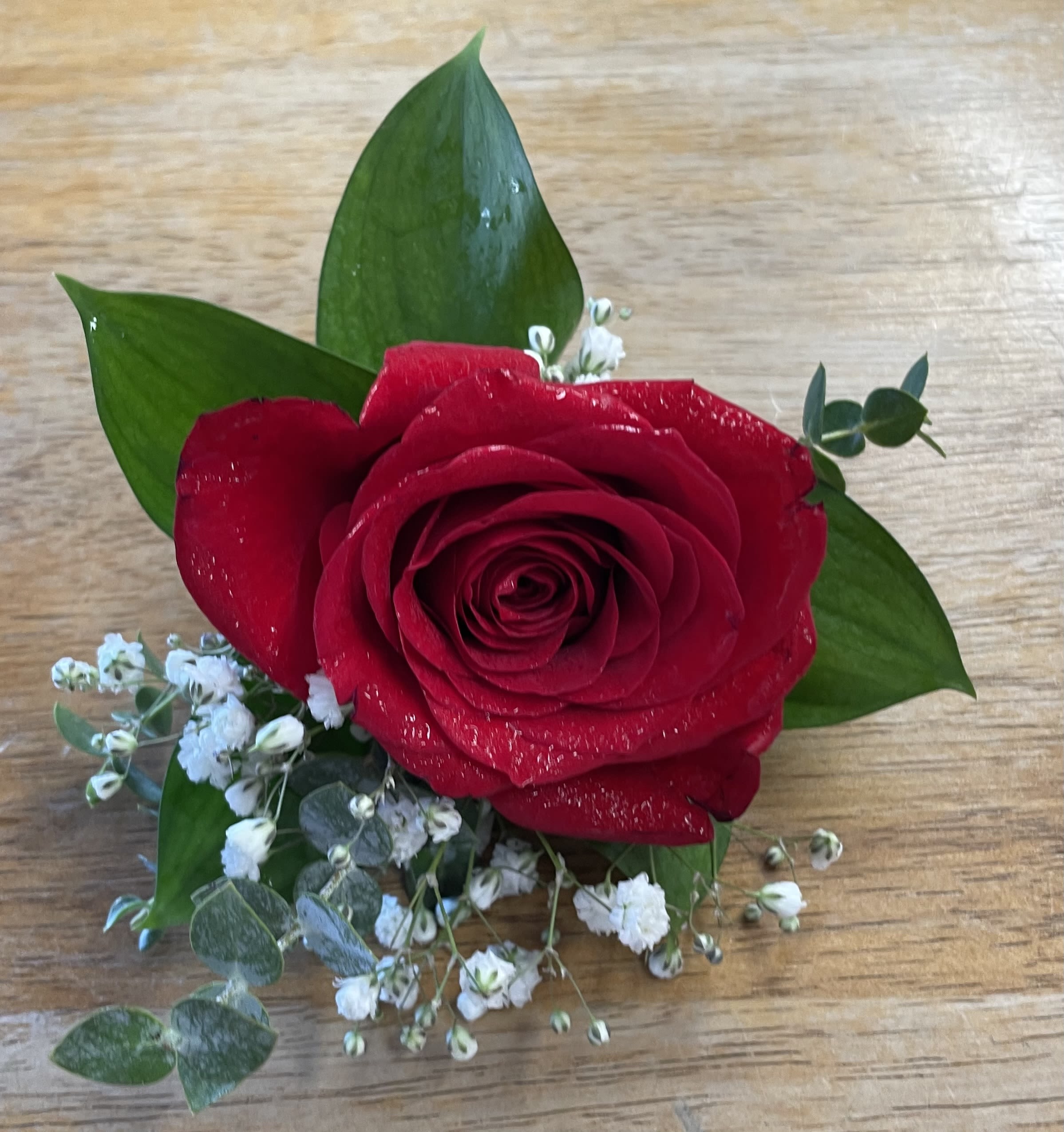 Single red rose with small white filler flowers and green leaves