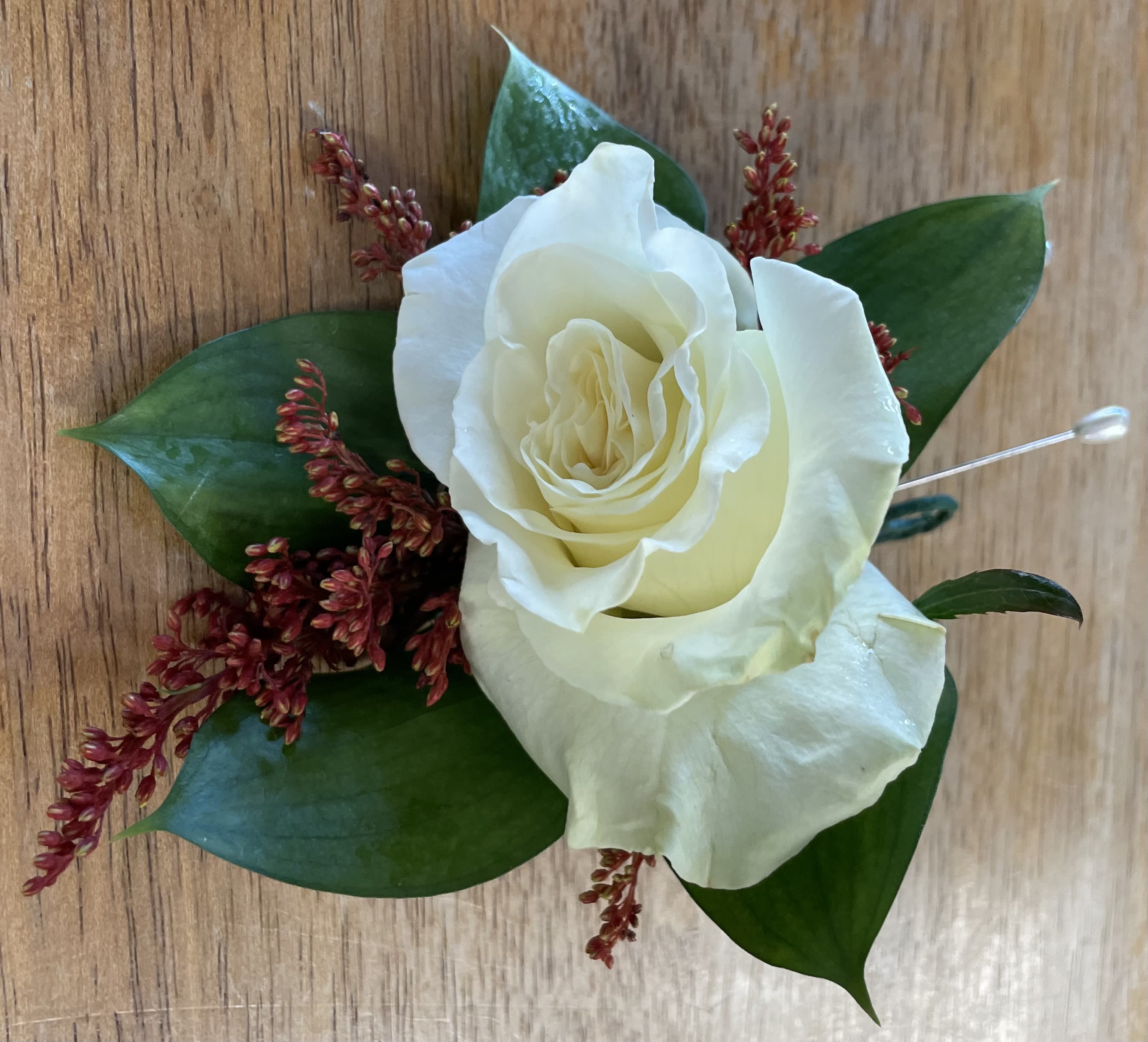 White rose boutonniere with dark green leaves and red filler flowers