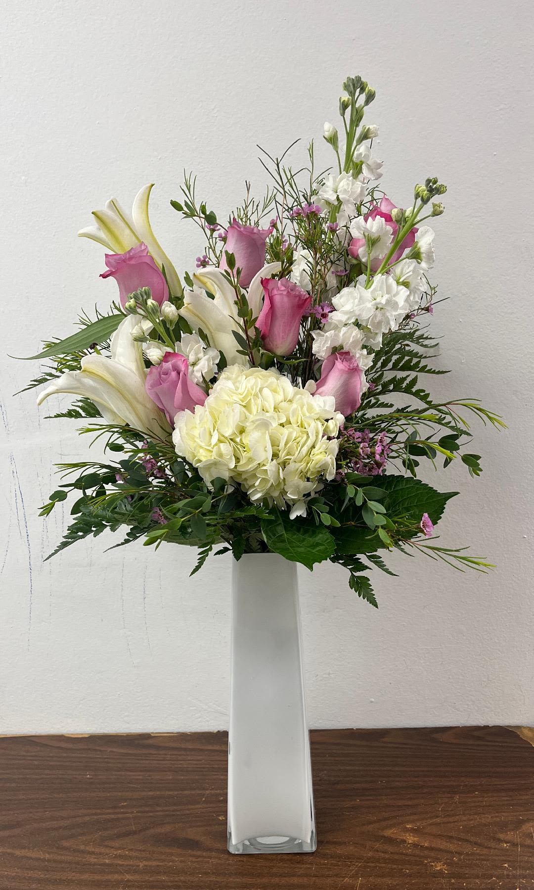 Pink roses and white lilies arranged in a tall white vase