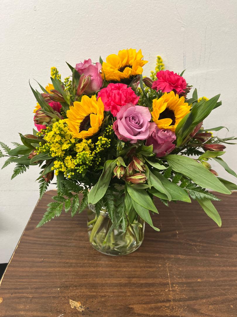 Mixed bouquet of sunflowers, roses, and carnations in a glass vase