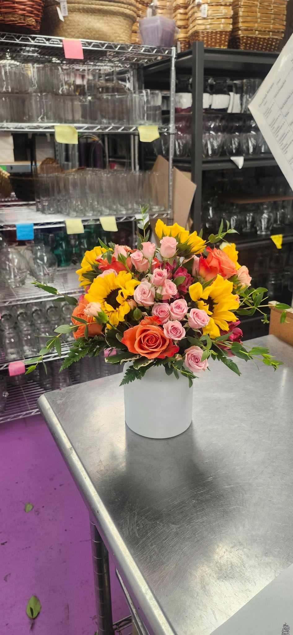 Sunset Serenade - A white vase filled with Sunflowers, spray roses, orange roses, Mini Carnations, Alstro, and Greens