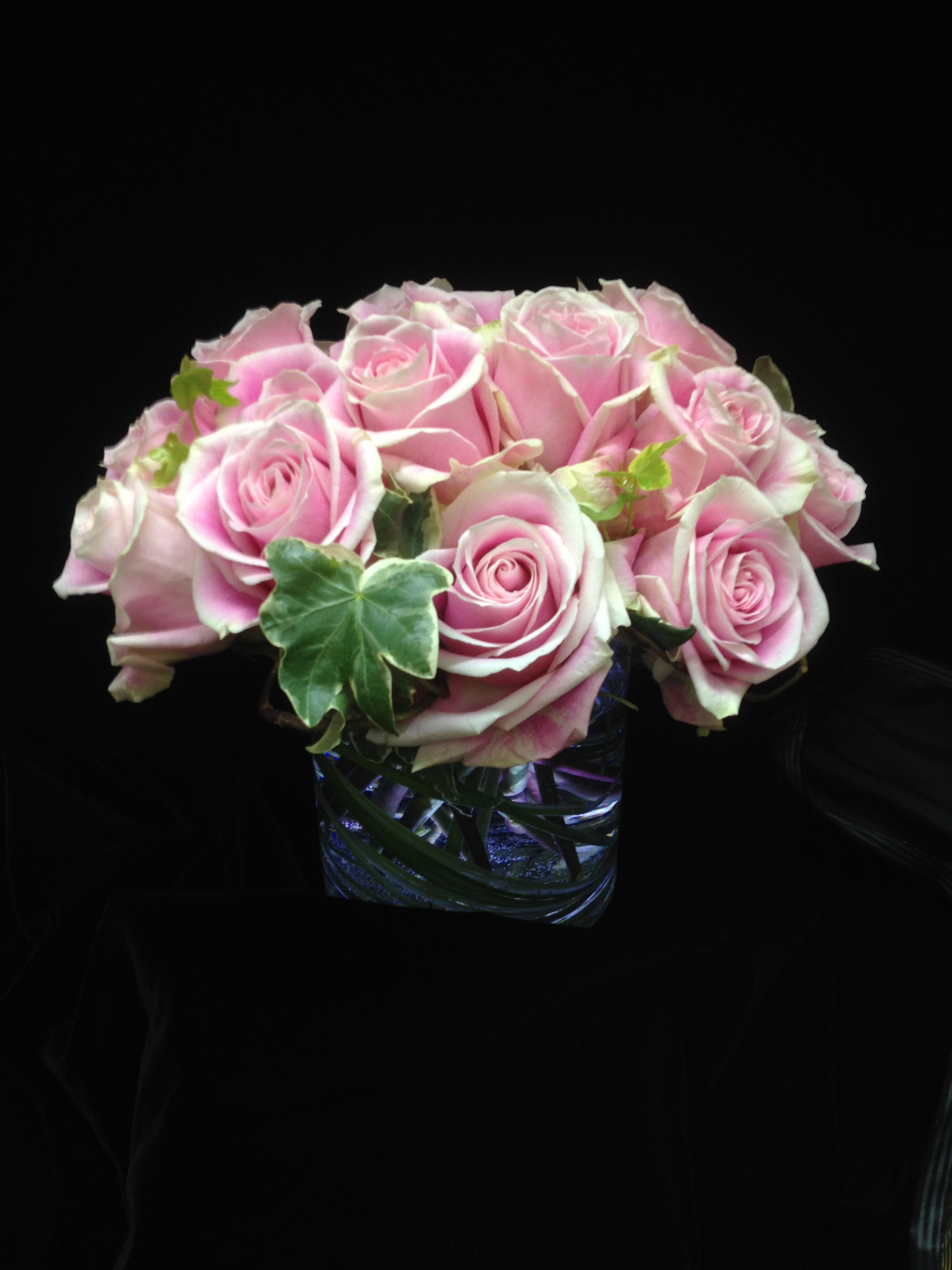 Low arrangement of pink roses with ivy accents in a clear glass cube vase