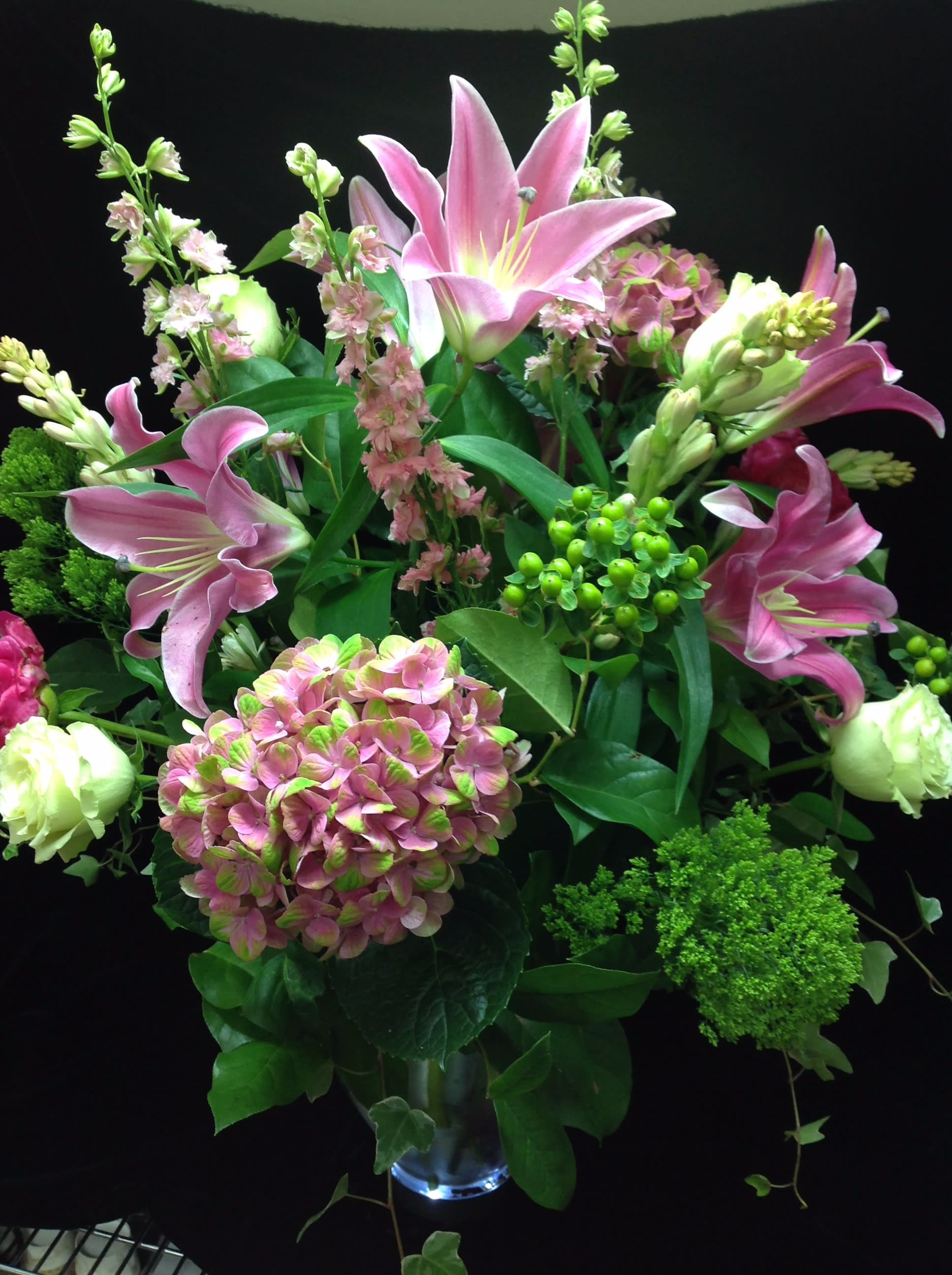 Tall arrangement of pink lilies and hydrangea with white blooms in a clear glass vase