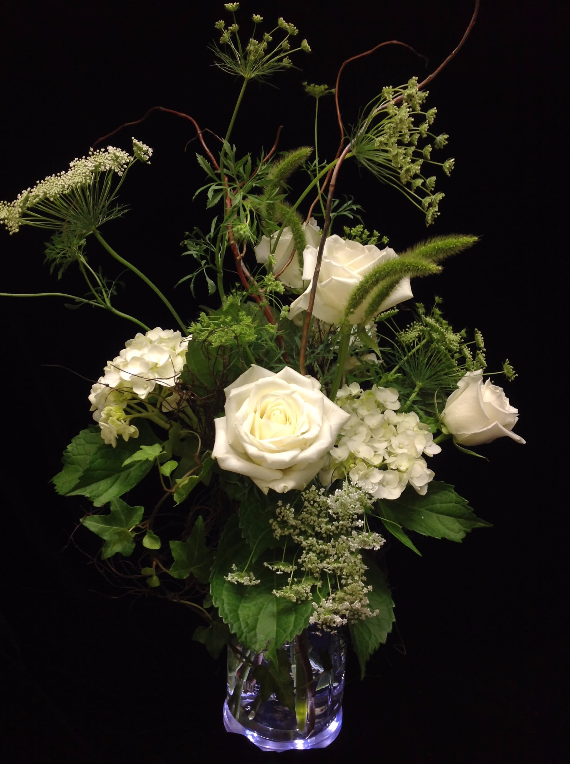 Tall arrangement of white roses and hydrangeas with airy filler in a clear glass vase
