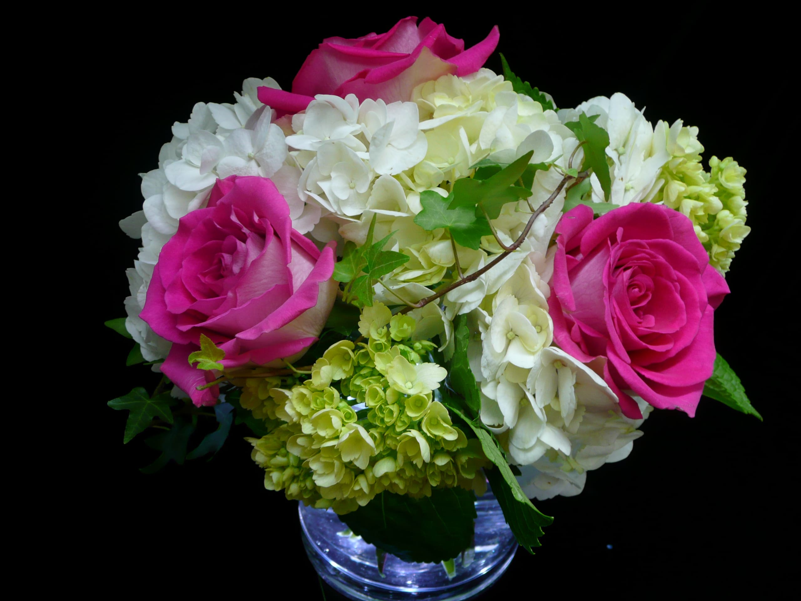 Compact arrangement of hot pink roses and white hydrangeas in a clear glass vase