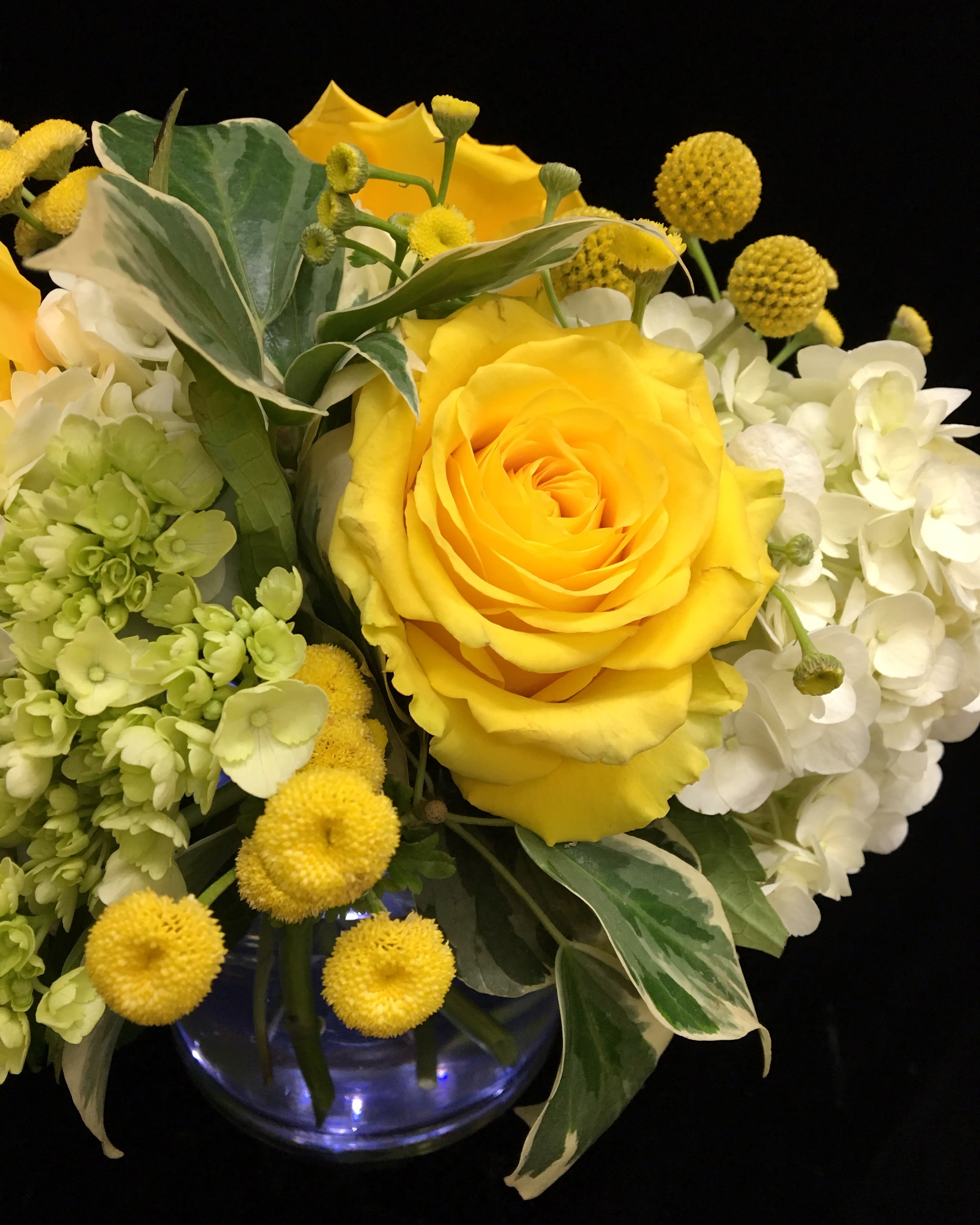 Yellow roses with white hydrangeas and round yellow blooms in a blue glass vase