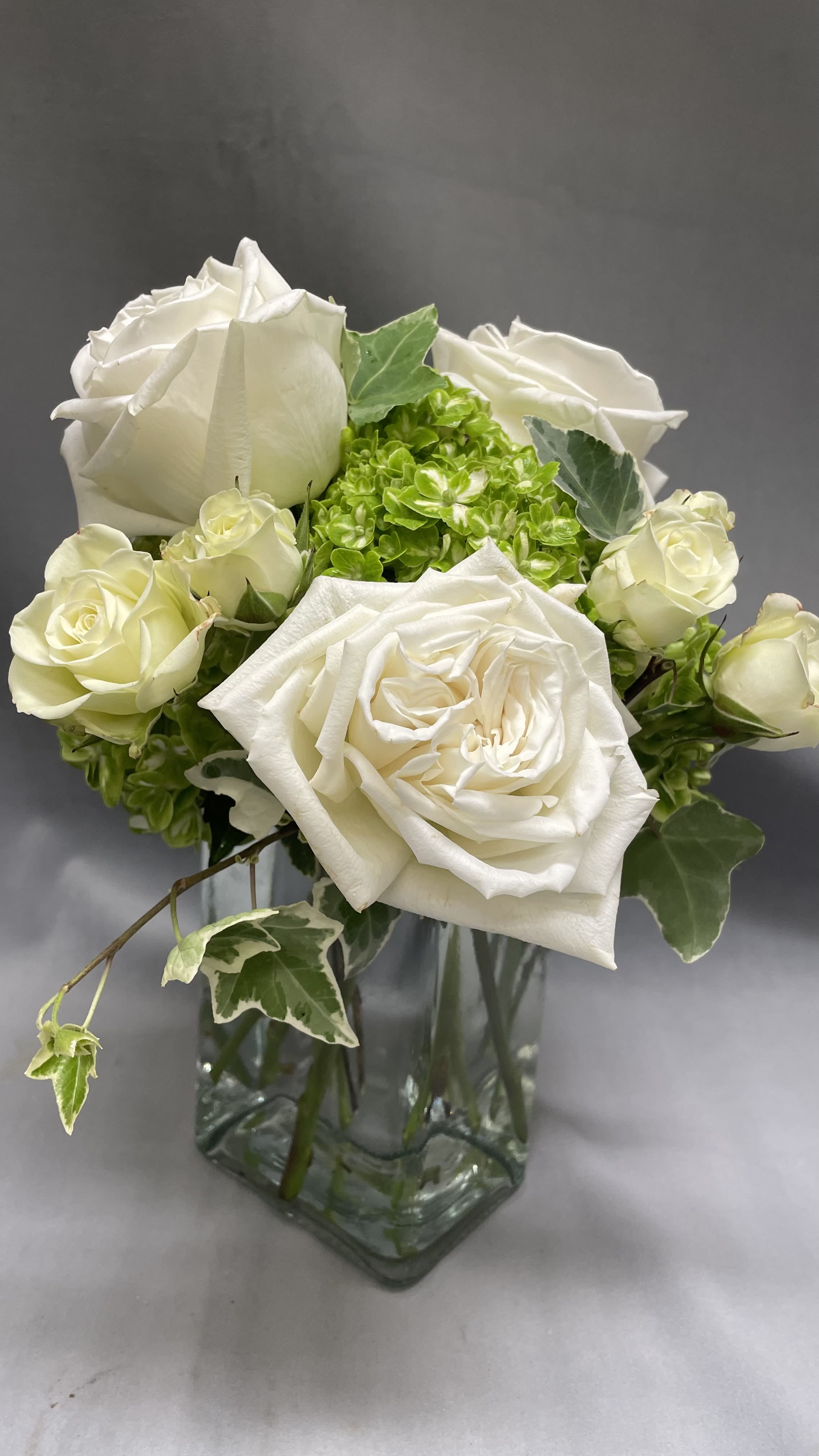 Small white rose and green hydrangea arrangement in a clear glass vase