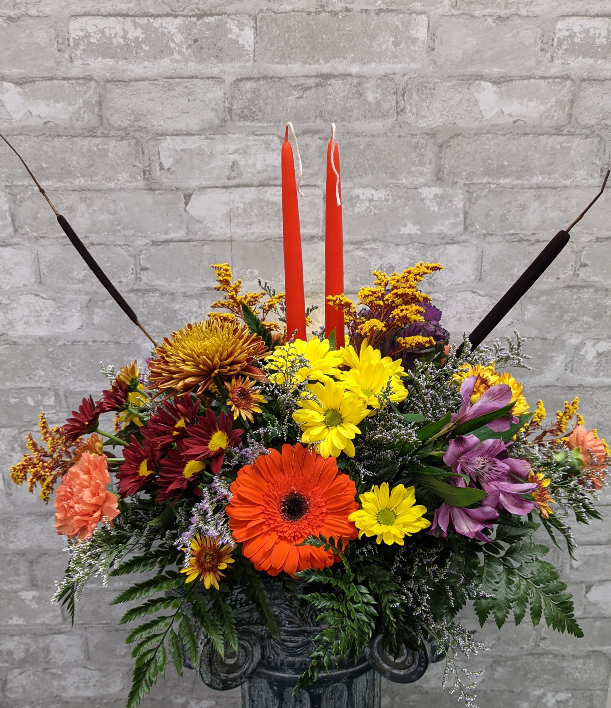 Colorful floral arrangement with two red candles in a dark container