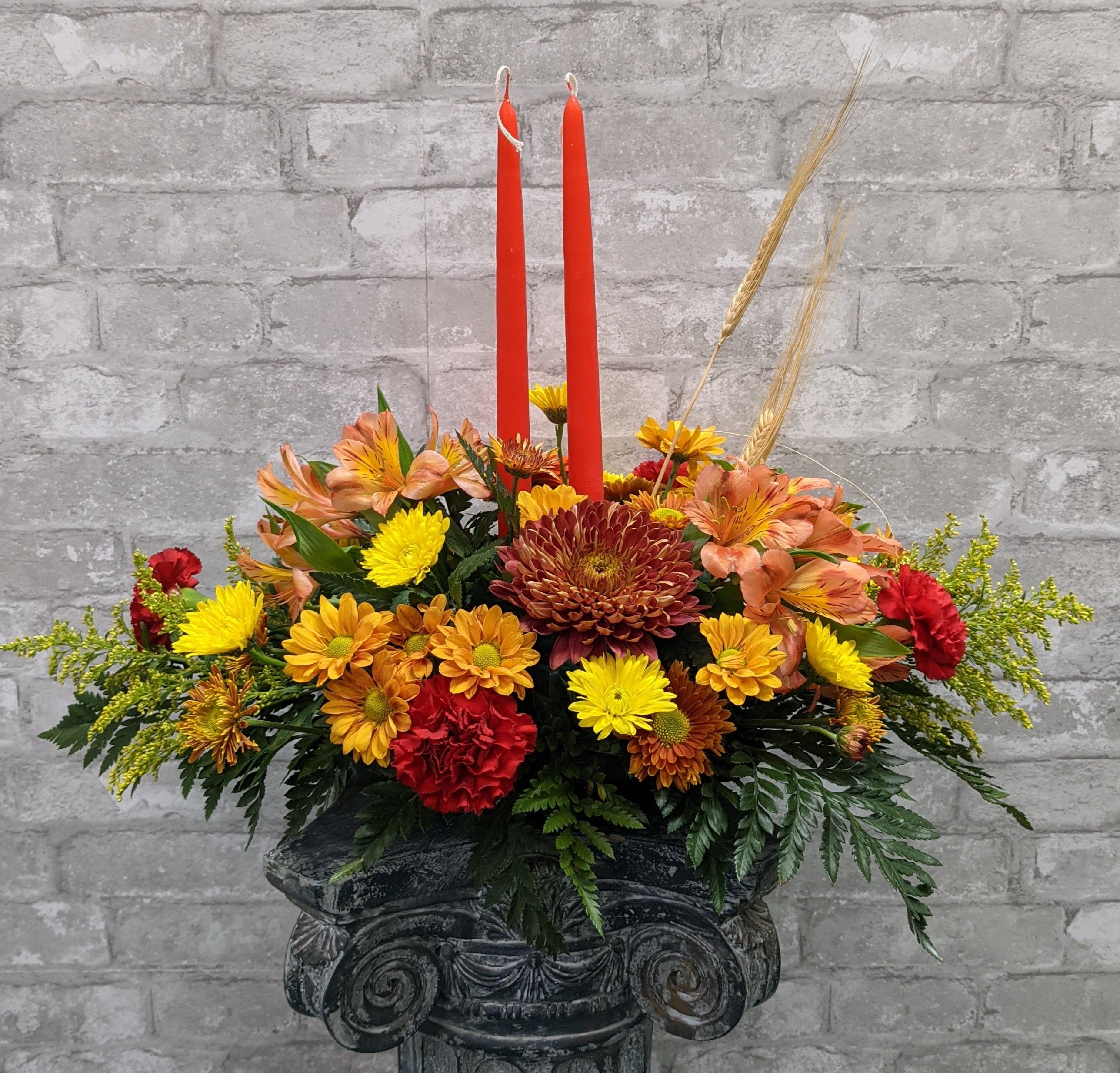 Autumn floral arrangement with red candles in a dark pedestal vase