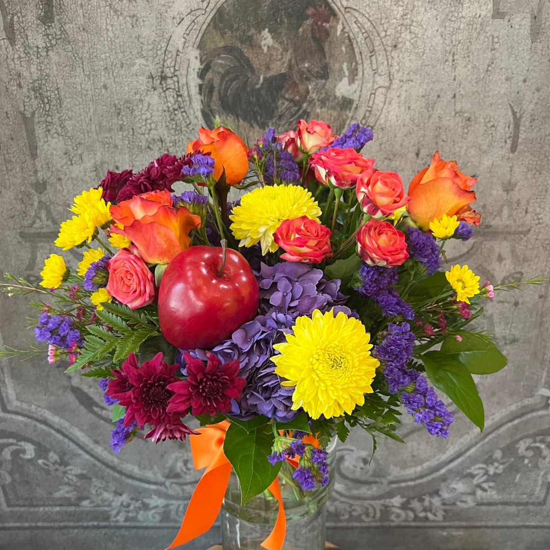 Colorful bouquet of roses, chrysanthemums, and hydrangeas in a glass vase with an apple