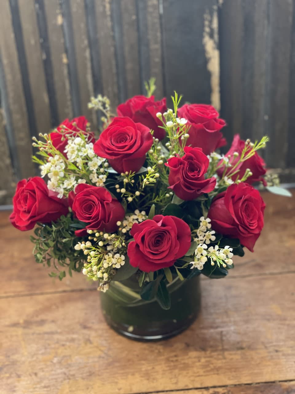 Red roses arranged in a dark glass vase with small white filler flowers