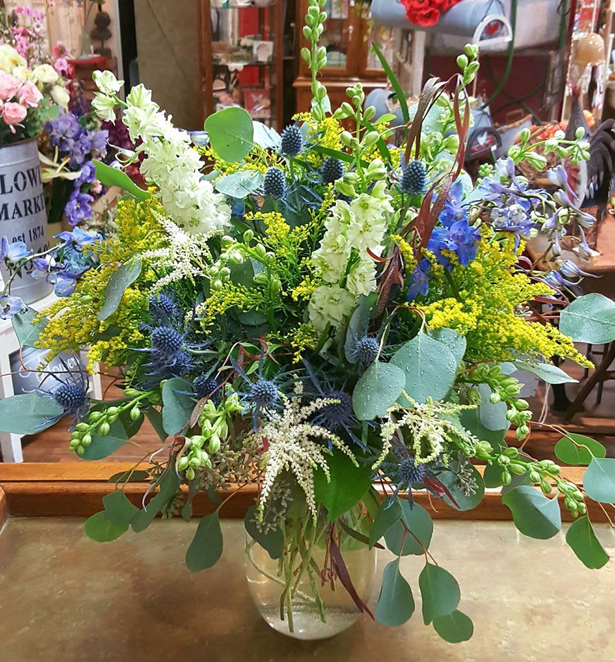 Mixed bouquet in a clear glass vase with blue, white, and yellow flowers
