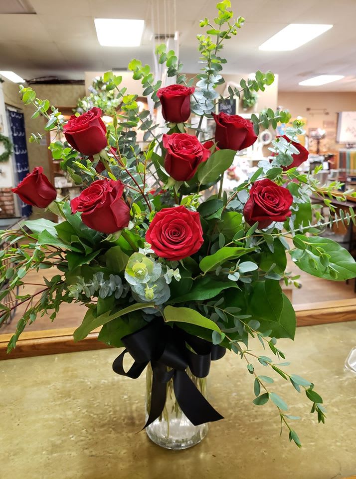 Red roses in a clear glass vase with greenery and a black ribbon