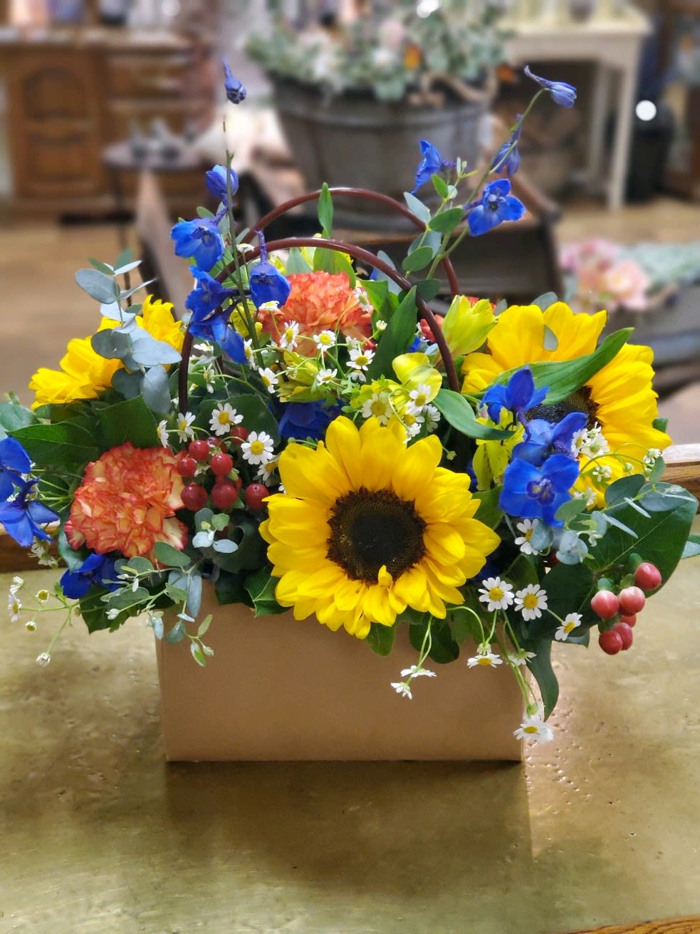 Bright sunflower arrangement in a cardboard box with blue and orange flowers