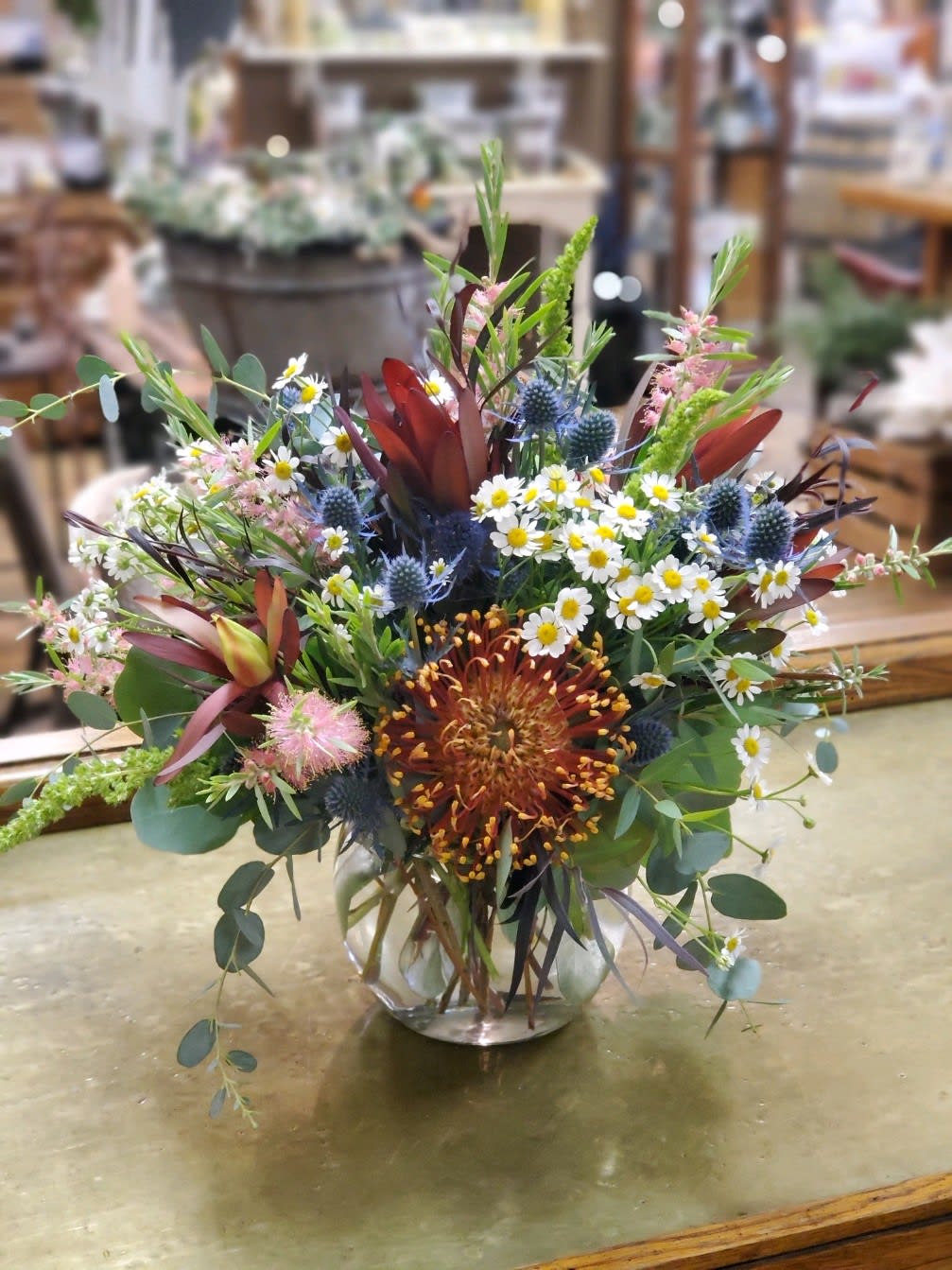 Mixed bouquet in a clear glass vase with daisies and spiky blue flowers