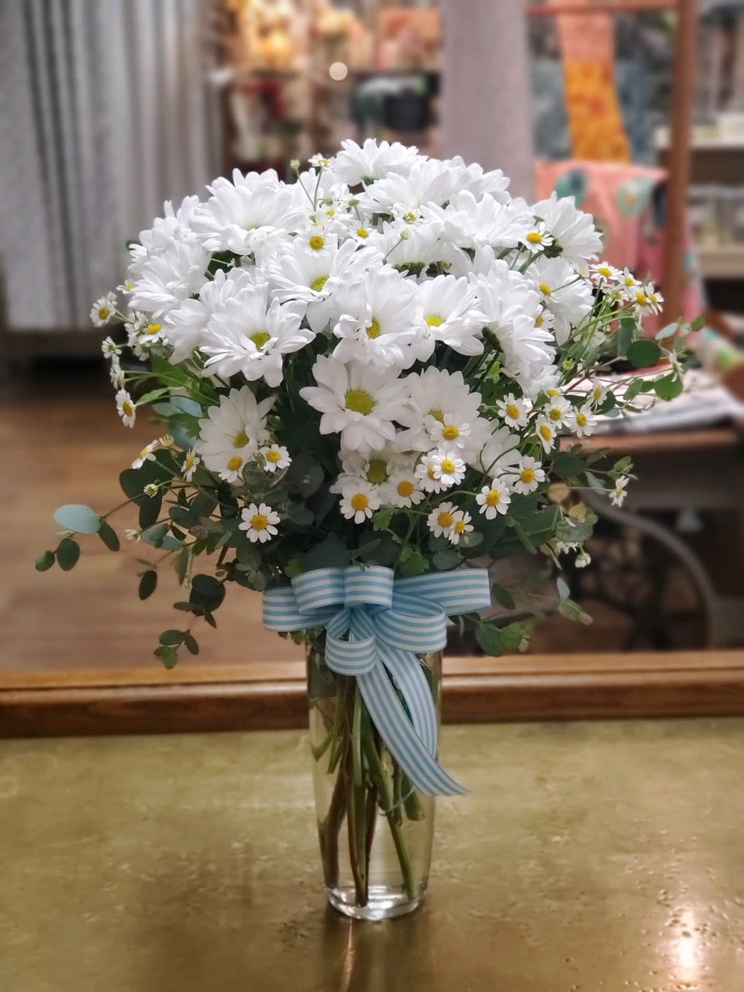 White daisy bouquet in a clear glass vase with a blue striped ribbon