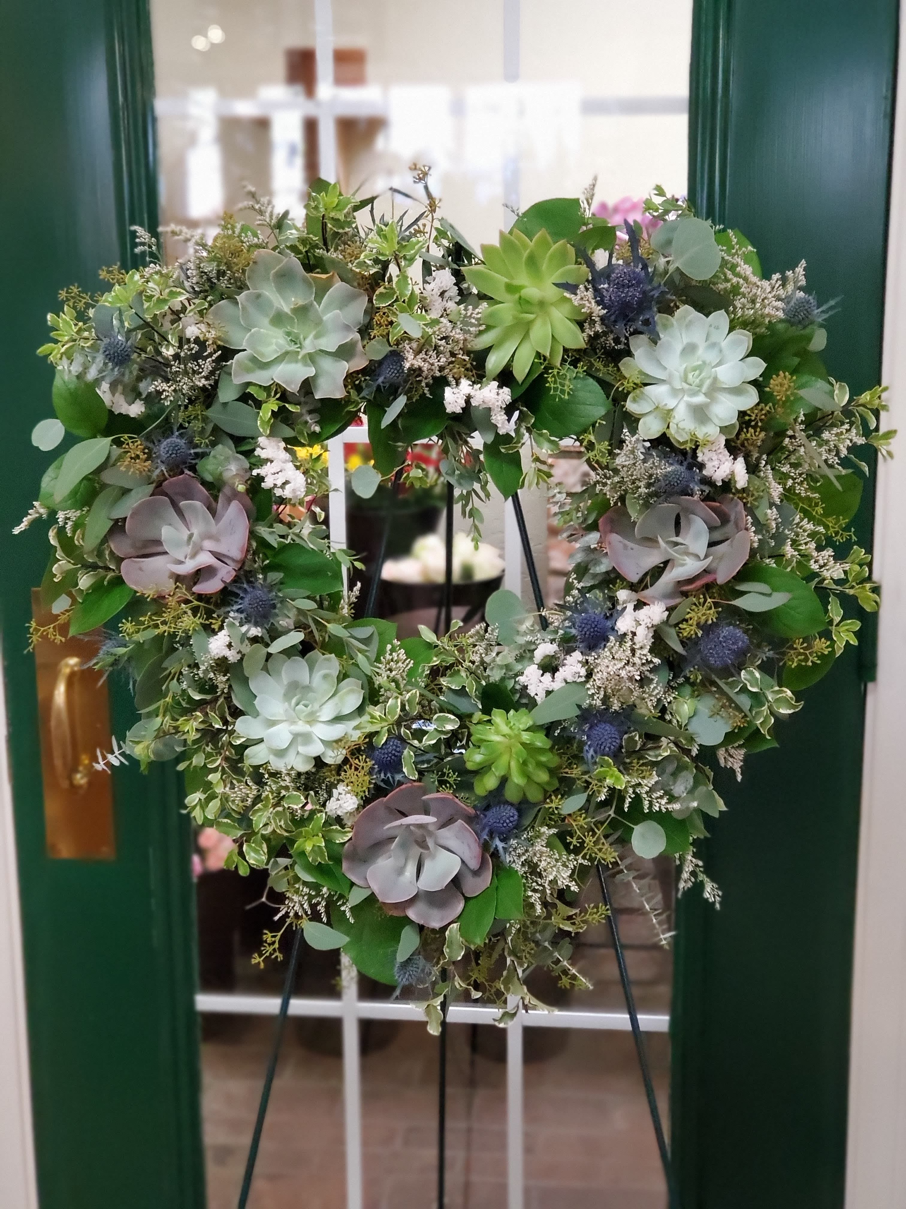 Heart-shaped succulent wreath on an easel with mixed greenery and blue accents