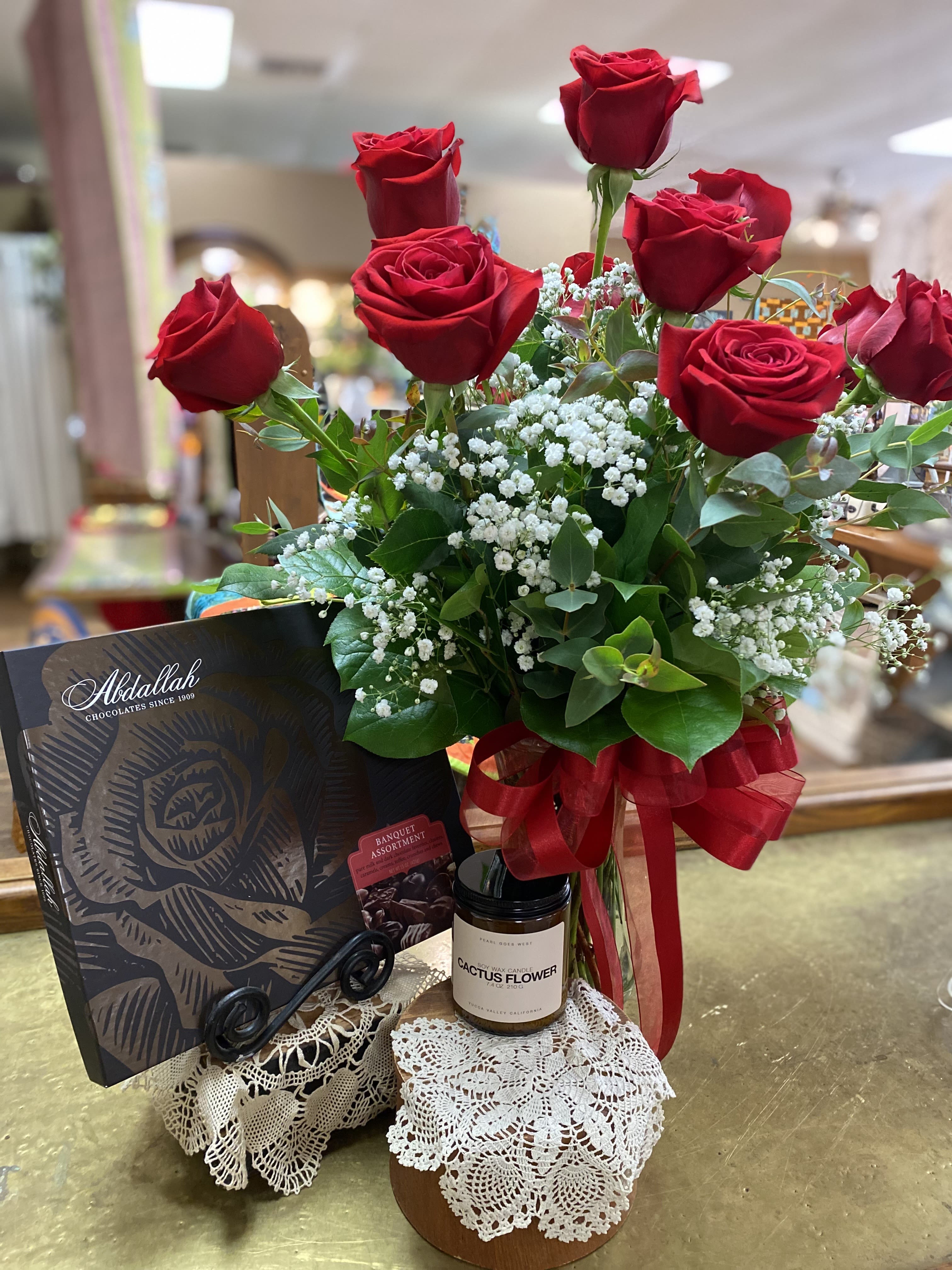 Red roses arranged with baby's breath, a chocolate box, and a candle